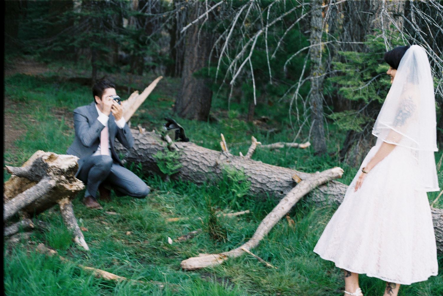 White wedding dress flowing in the wind against rustic wooden logs in a forest setting.