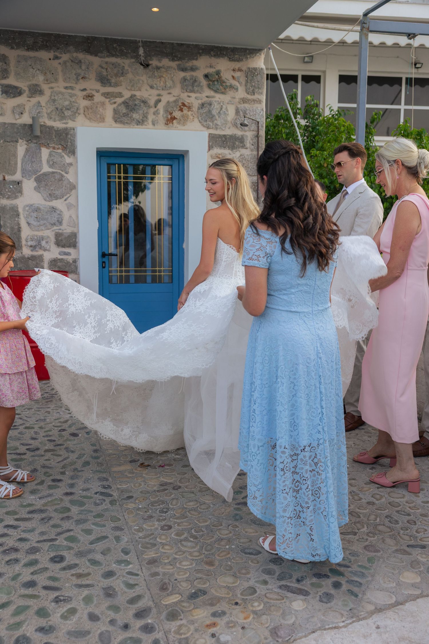 Wedding party helping with a bride's dress outside a stone building with a blue door.