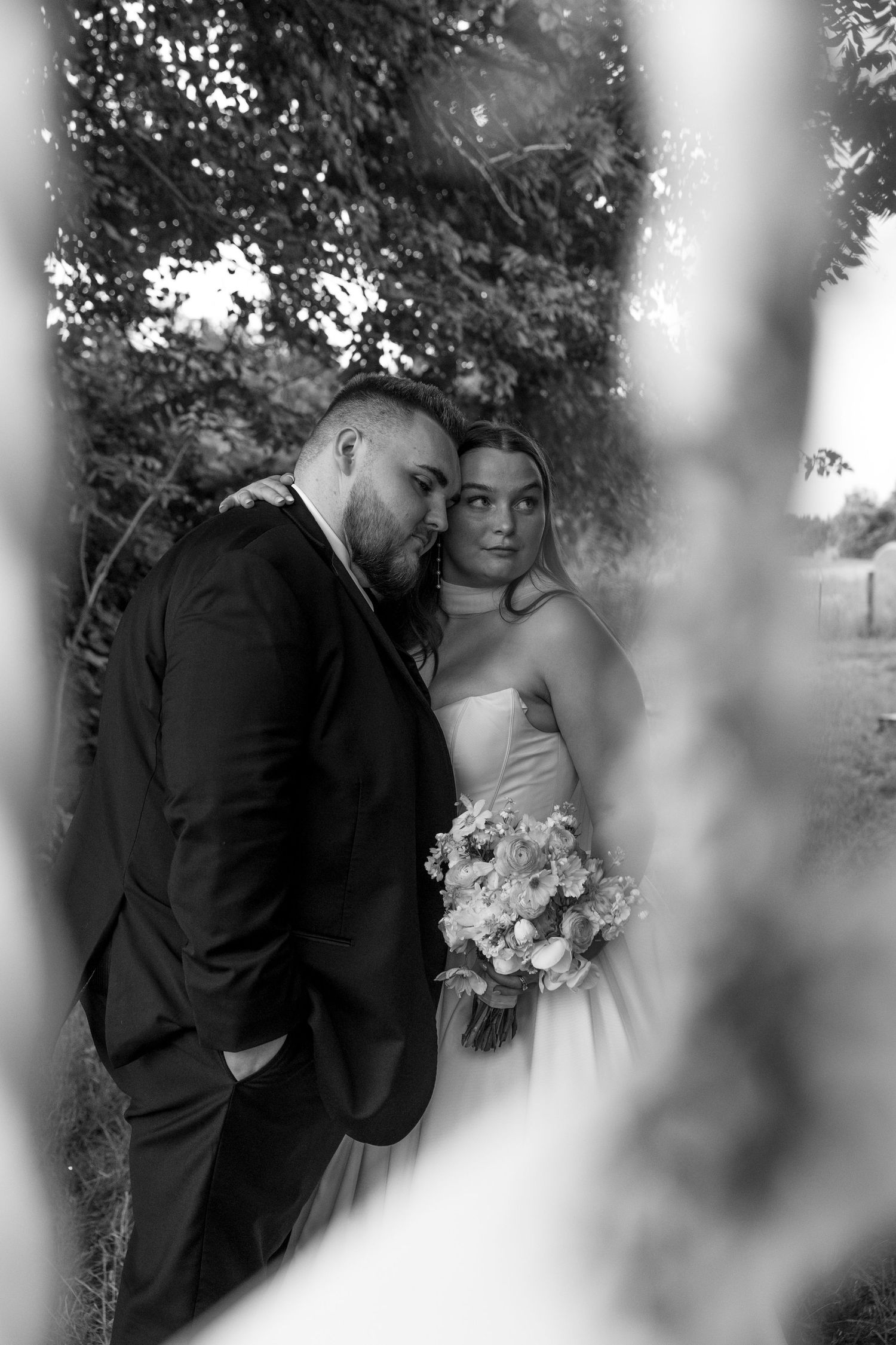 An artistic black and white wedding portrait captured through natural foliage.