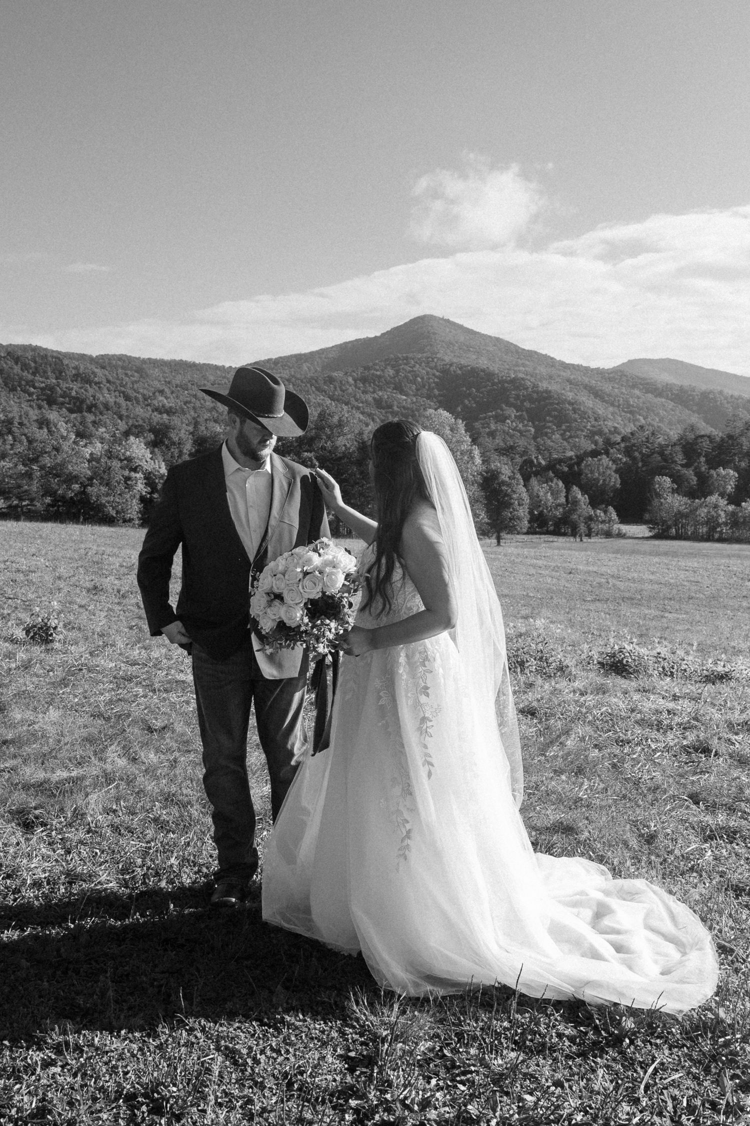 Black and white wedding photos of a couple in a scenic mountain meadow with rolling hills and trees in the background.