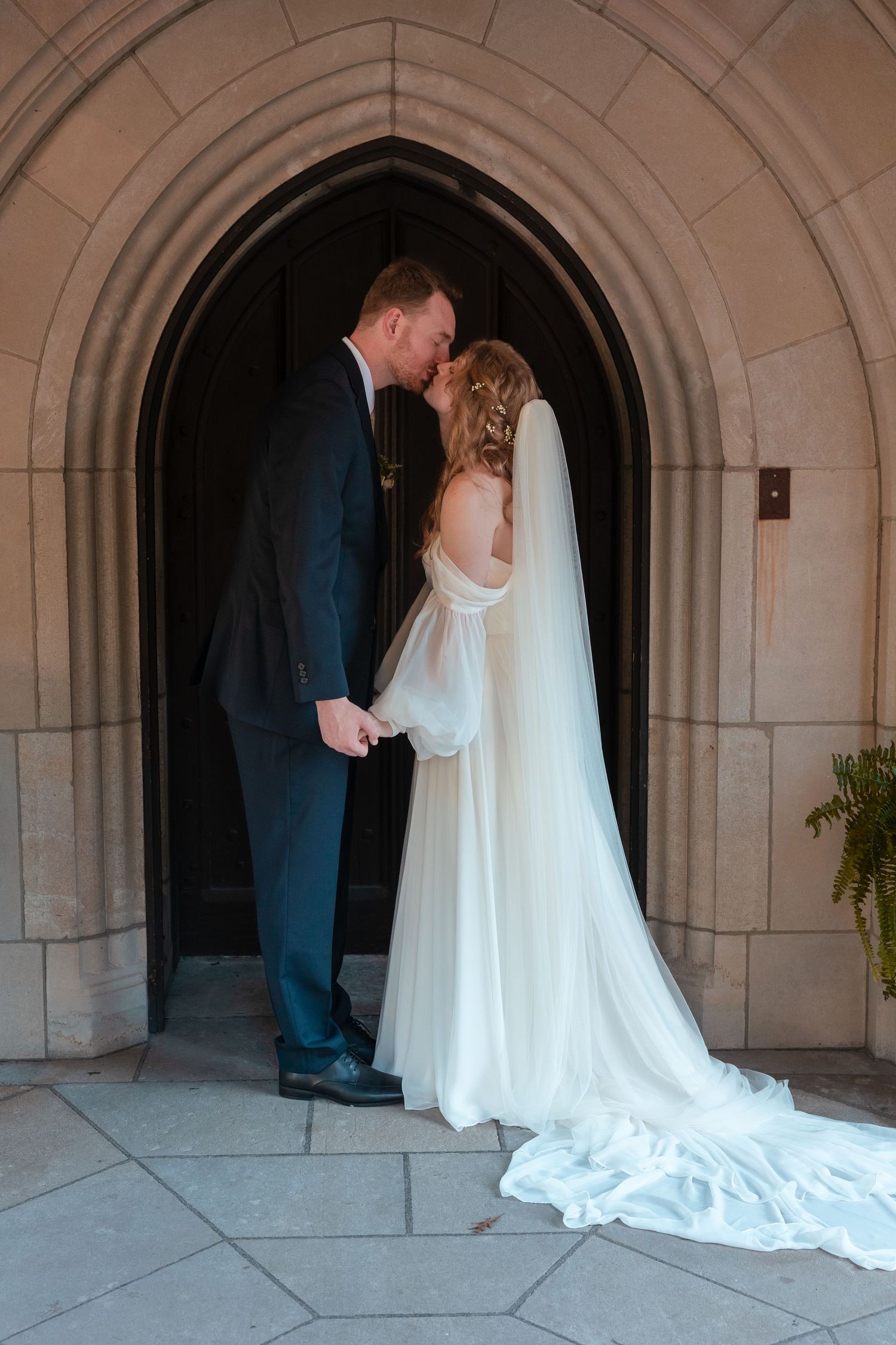 Wedding couple poses in elegant stone archway for romantic first look photos.