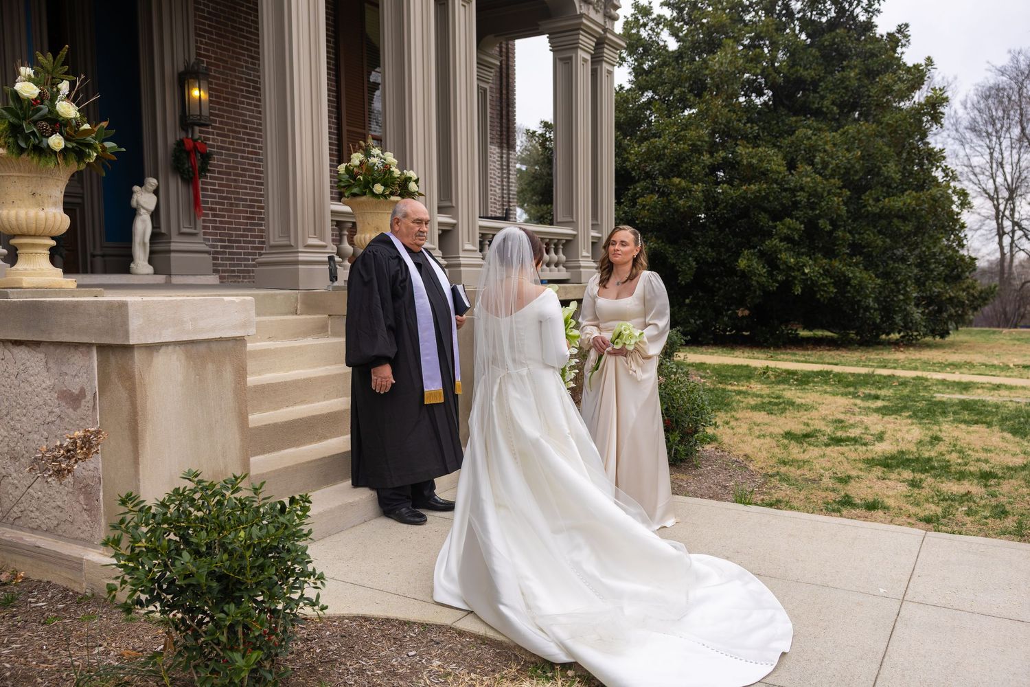 A wedding ceremony takes place on elegant stone steps with floral arrangements and columns framing the entrance.