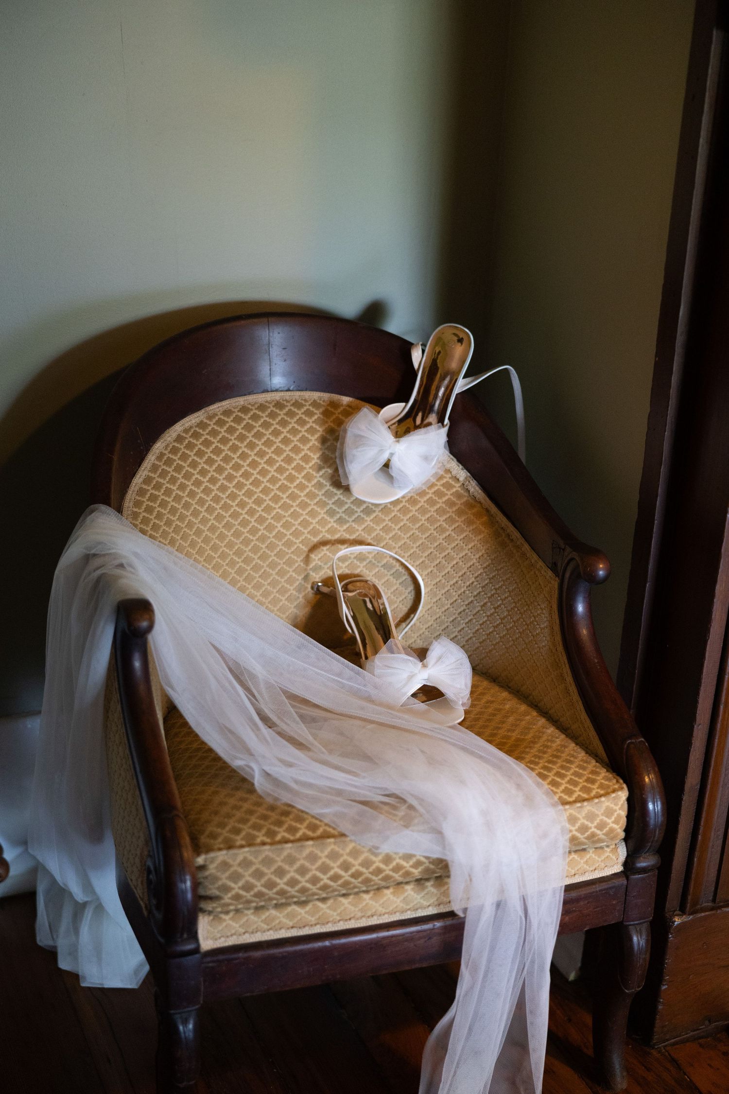 A delicate white wedding veil draped across an antique upholstered chair.