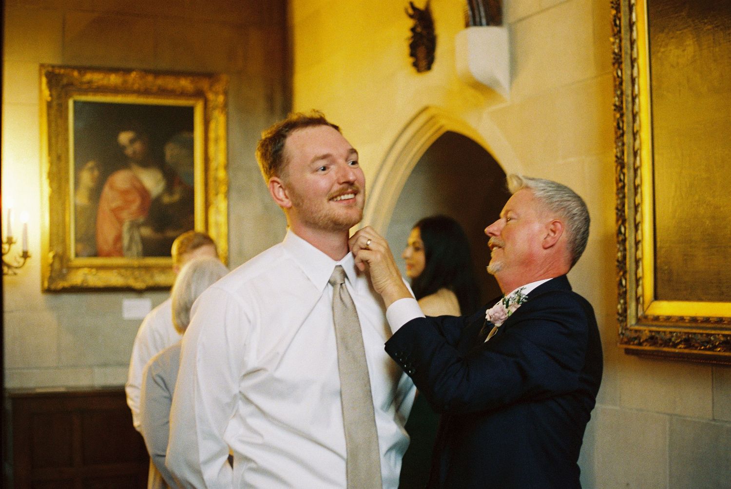 Two people share a candid moment of laughter in an elegant room with gold-framed paintings on the wall.