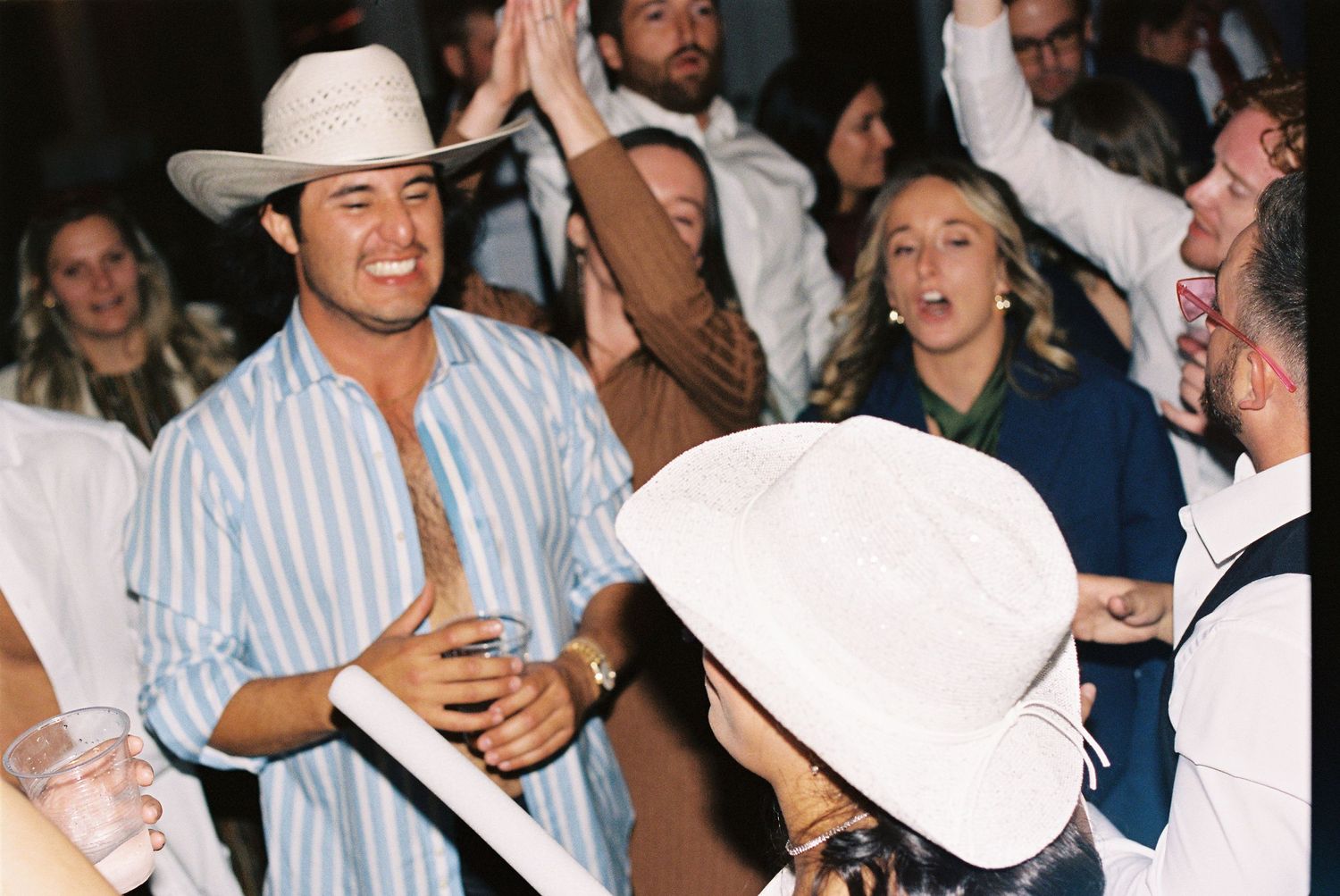 Party guests dancing and celebrating at a reception while wearing western-style cowboy hats.