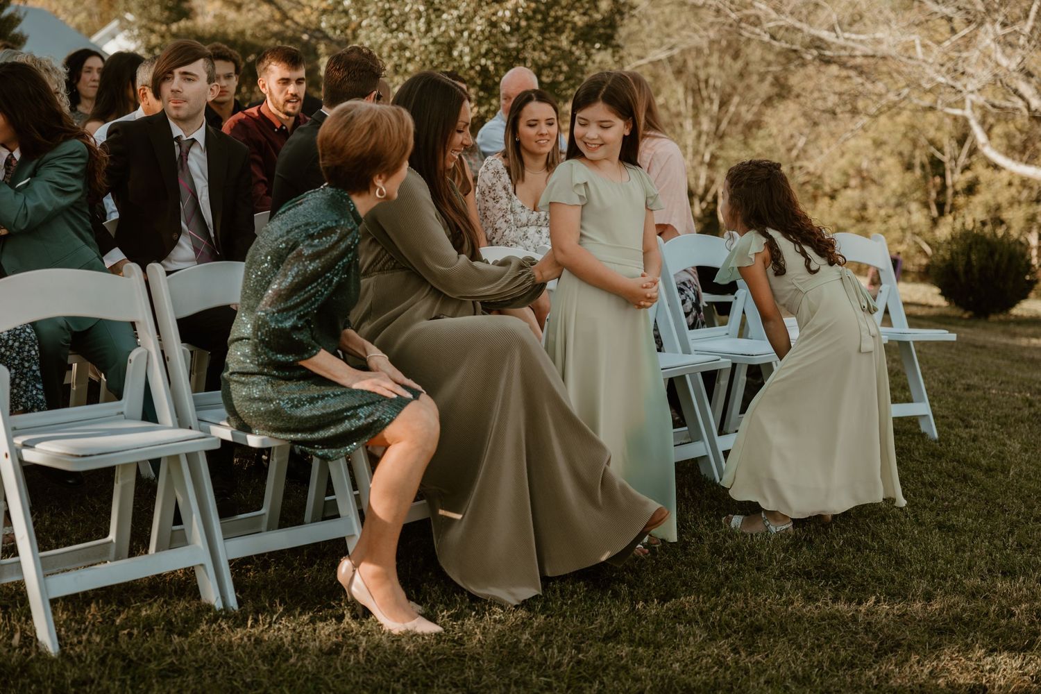 Wedding guests seated in white chairs on a lawn during an outdoor ceremony.