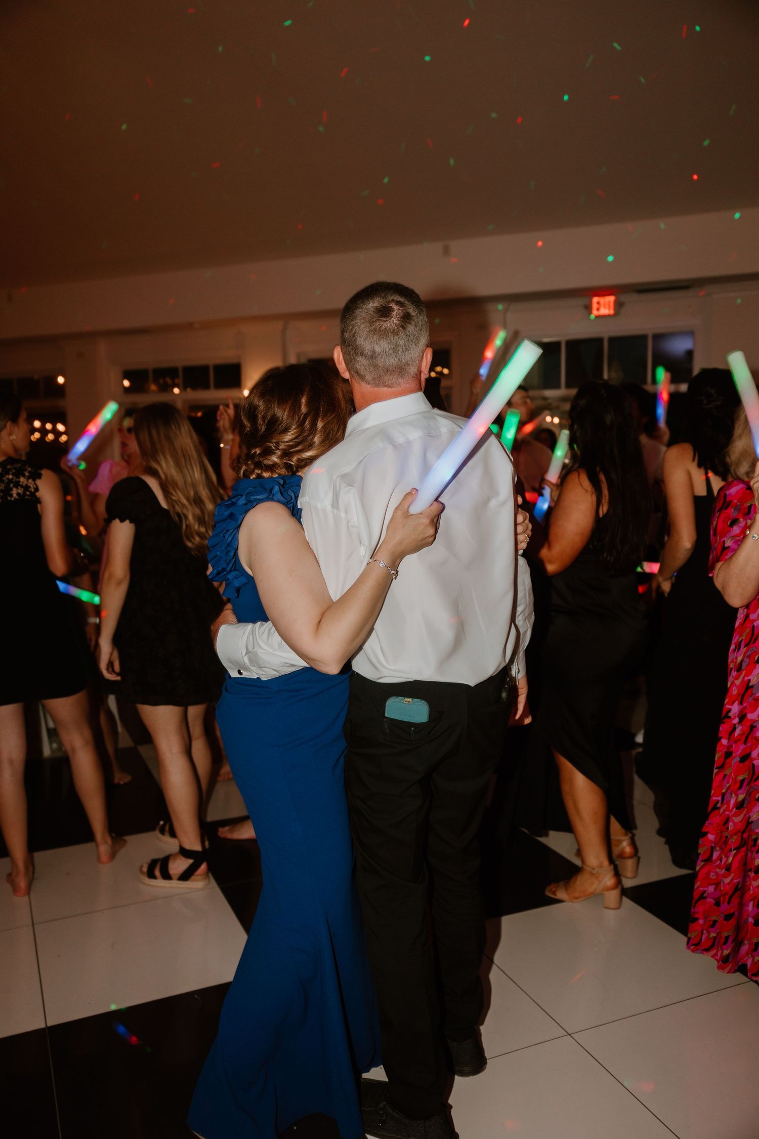 Dancers move on an illuminated dance floor with colorful lights during a wedding reception.