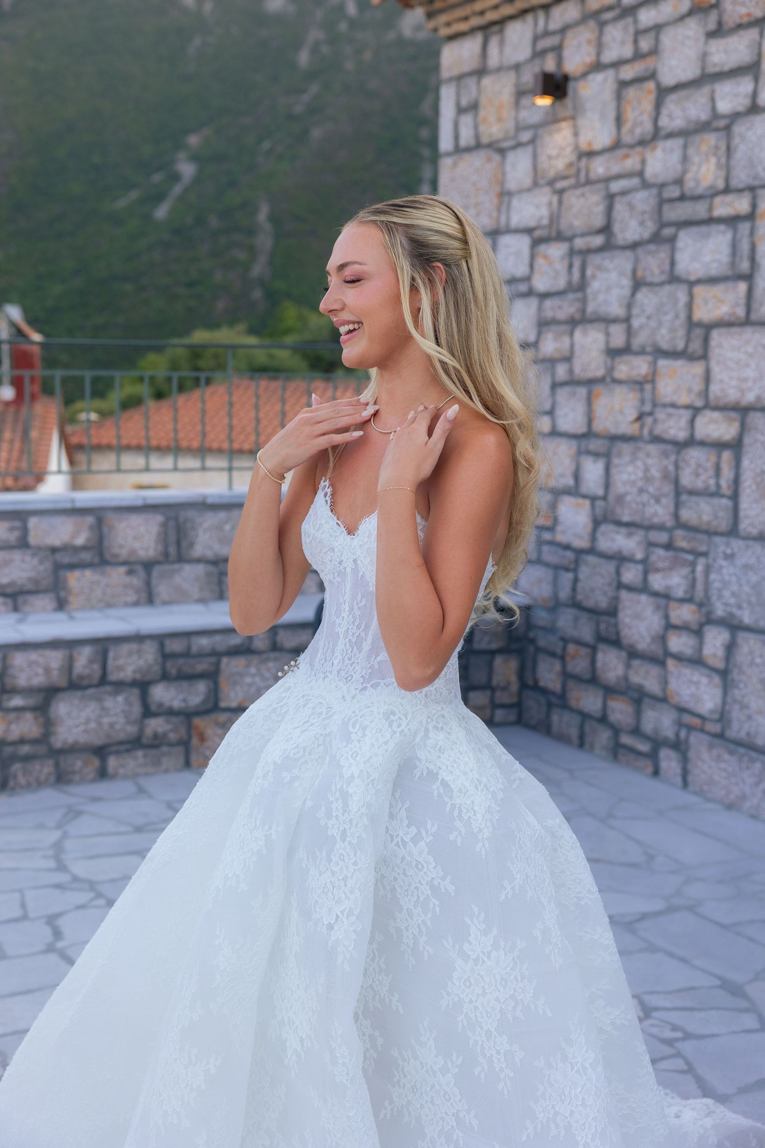 A bride in a white lace ball gown poses gracefully against a stone wall backdrop.