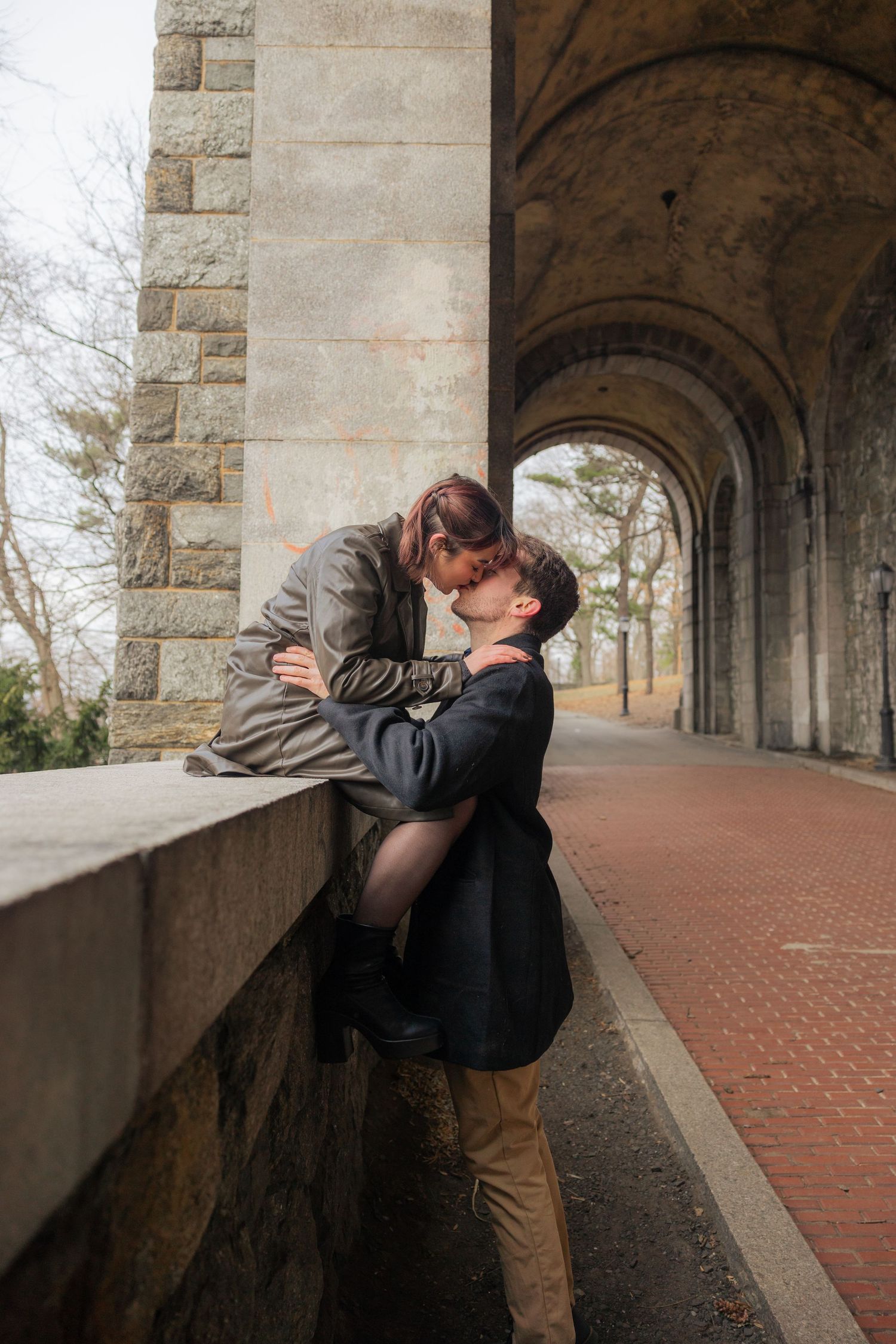 A romantic moment shared between a couple under stone archways along a brick pathway.