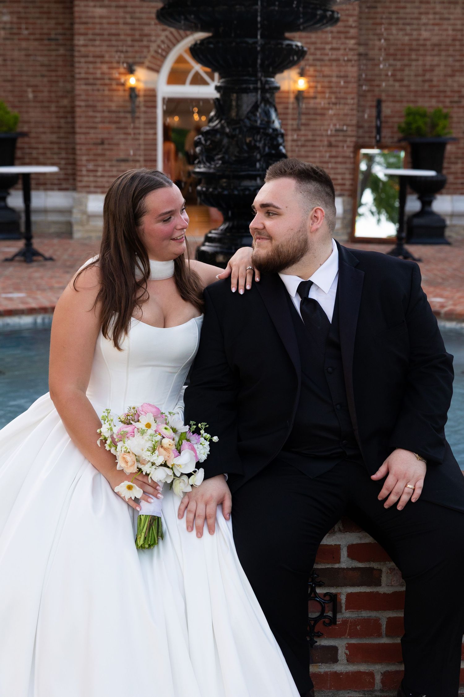 A romantic wedding portrait on a brick patio with a decorative fountain in the background.