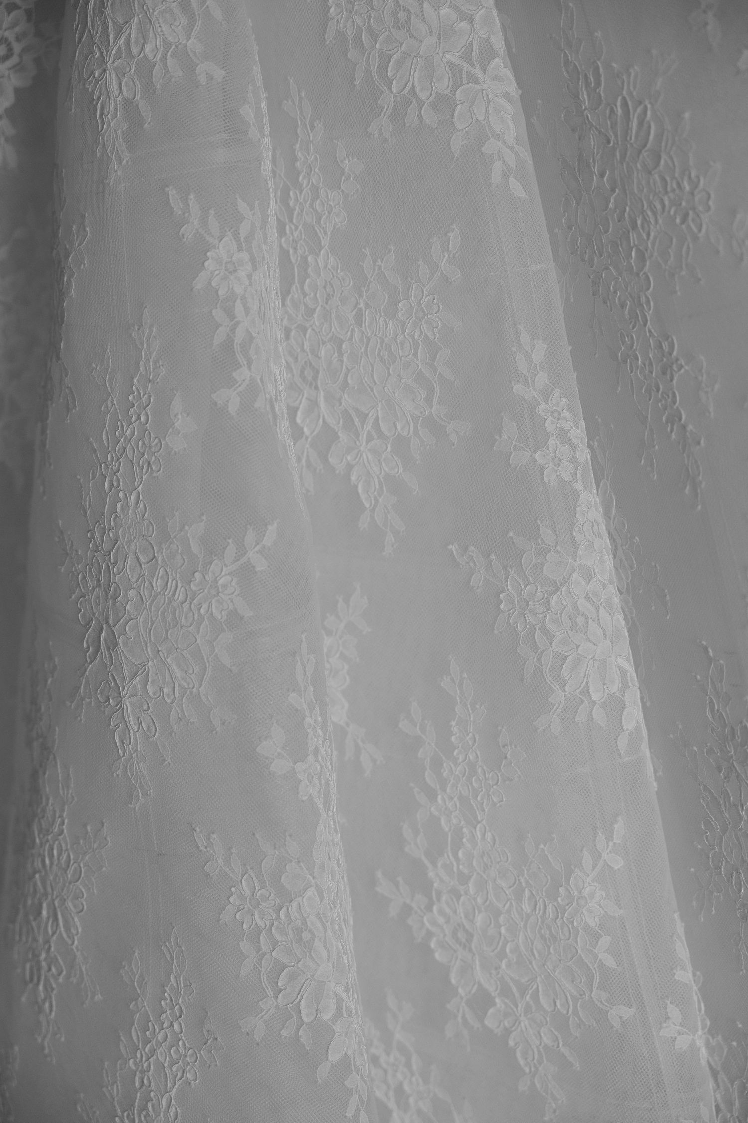 Delicate white lace fabric with intricate floral patterns creates an elegant textured background.