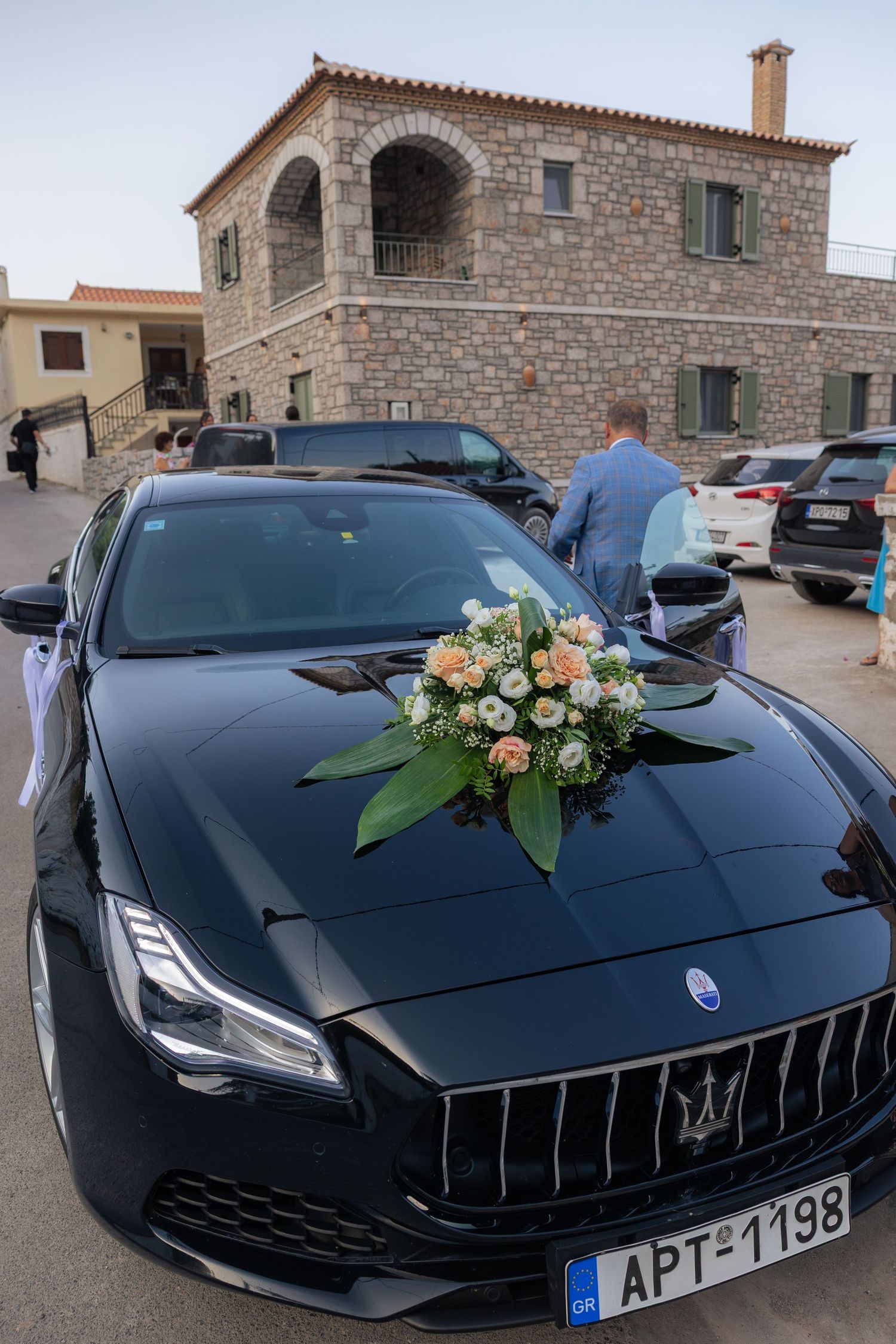 Black Maserati luxury car decorated with elegant floral arrangements on its hood parked outside stone buildings.