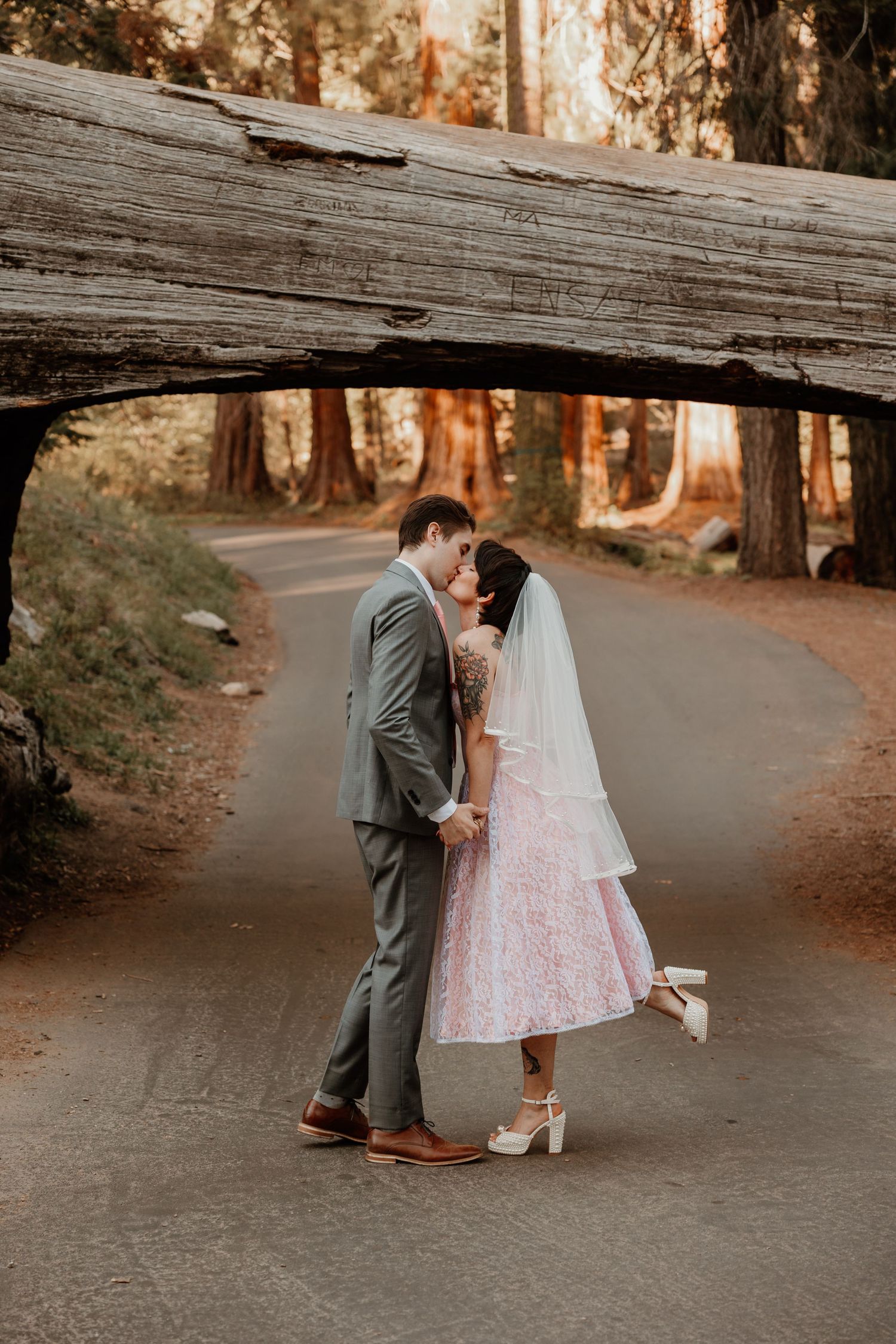 A romantic wedding moment under a fallen log tunnel in a forest setting.