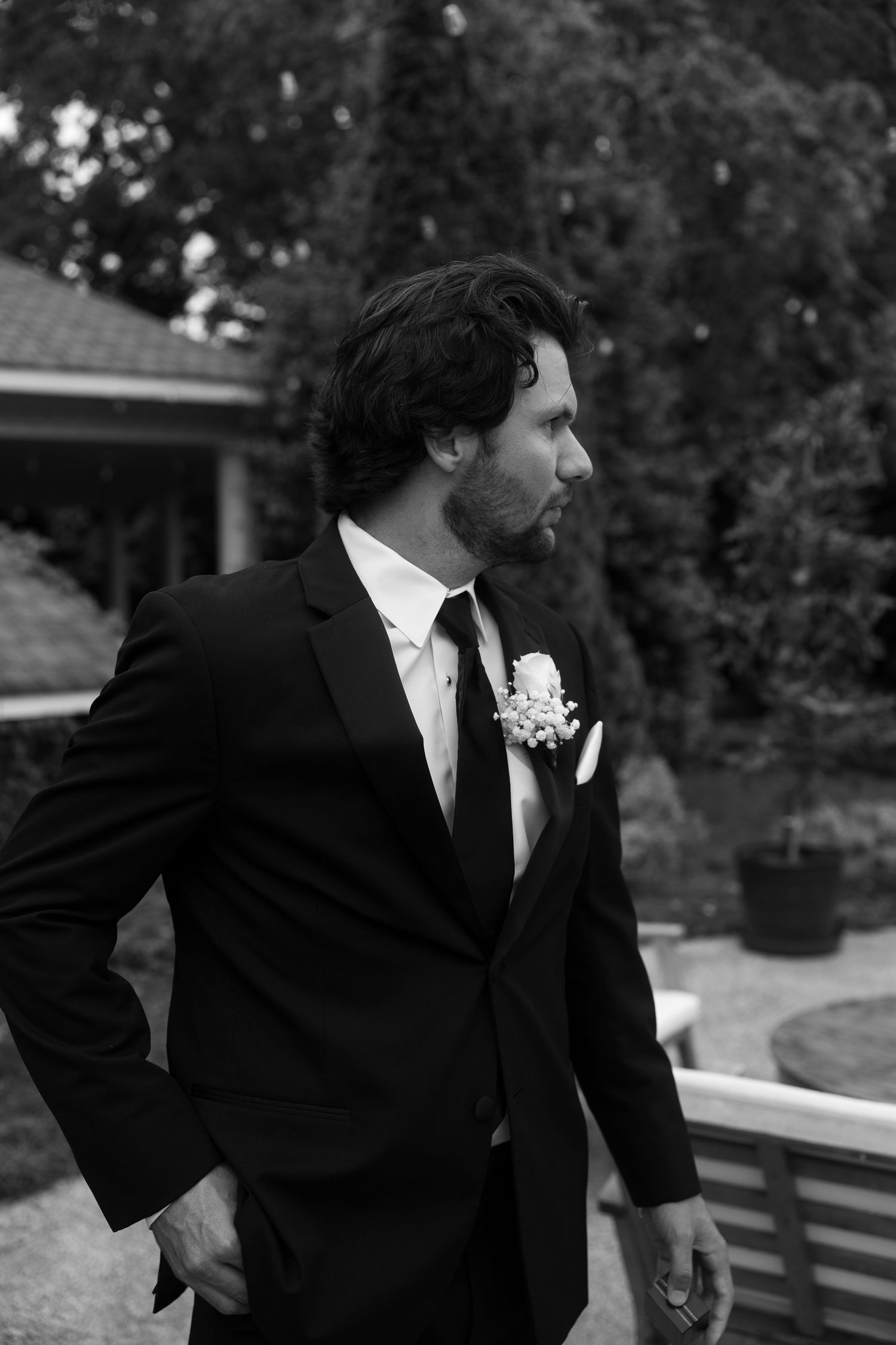 A side view of groomsmen in formal black suits and ties at an outdoor wedding.