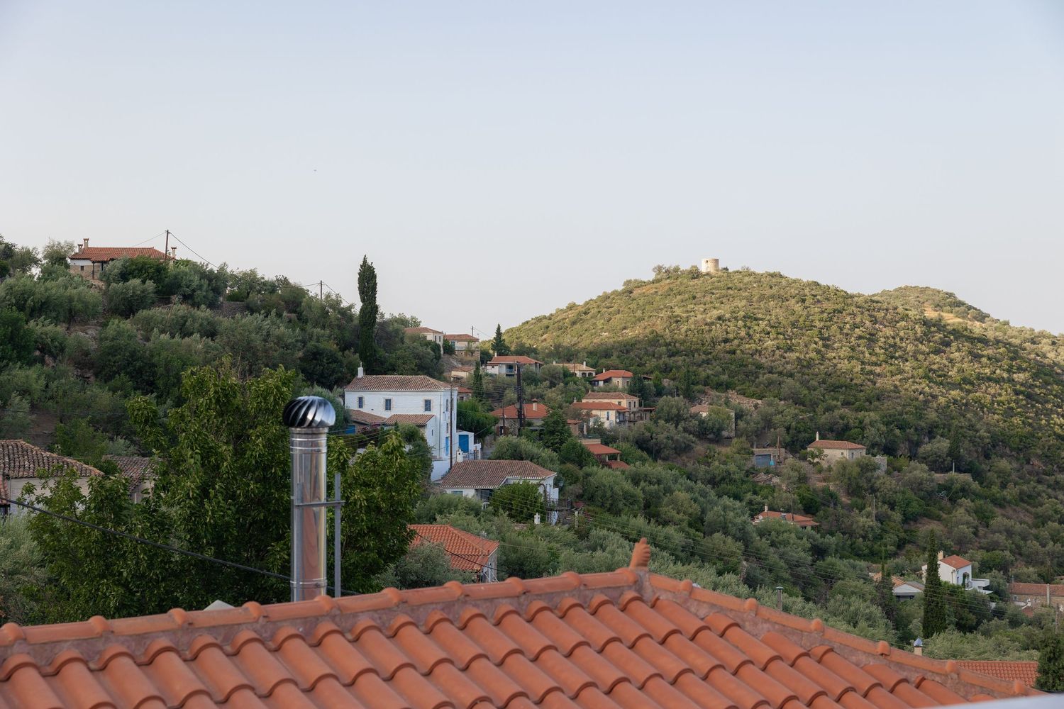 Scenic mountain landscape with terracotta rooftops and olive groves under a clear blue sky.