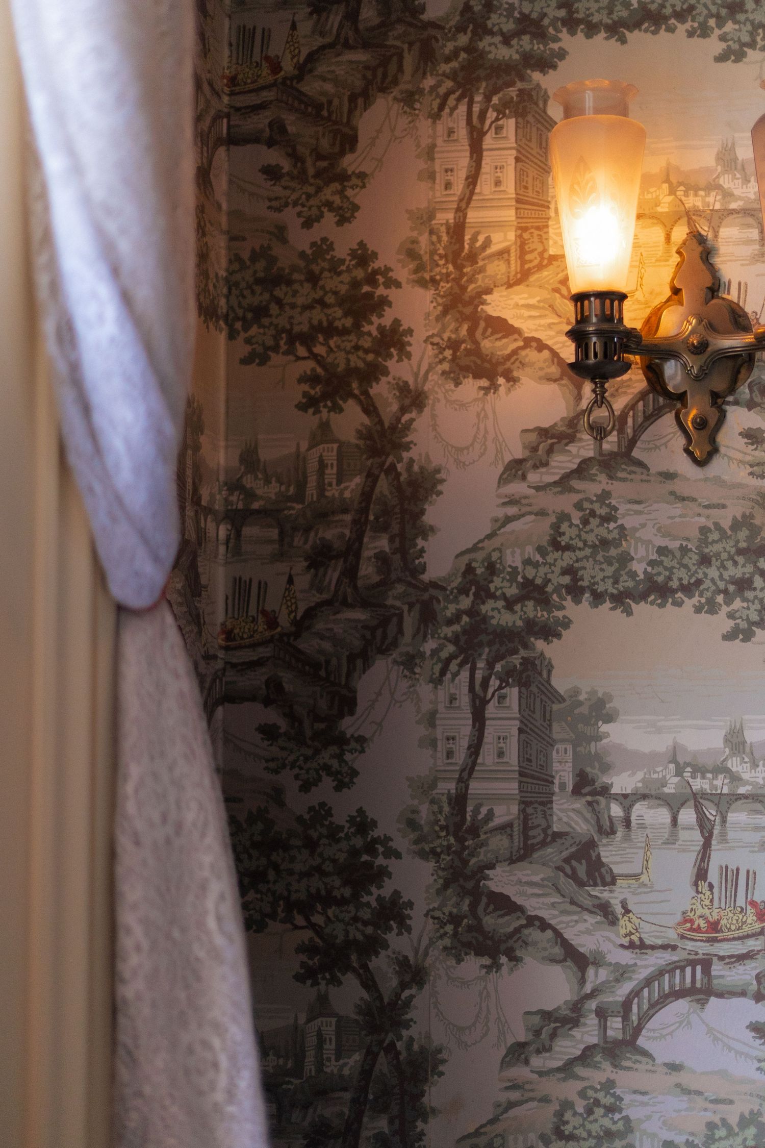 Vintage toile wallpaper with pastoral scenes illuminated by warm lighting in an elegant interior setting.