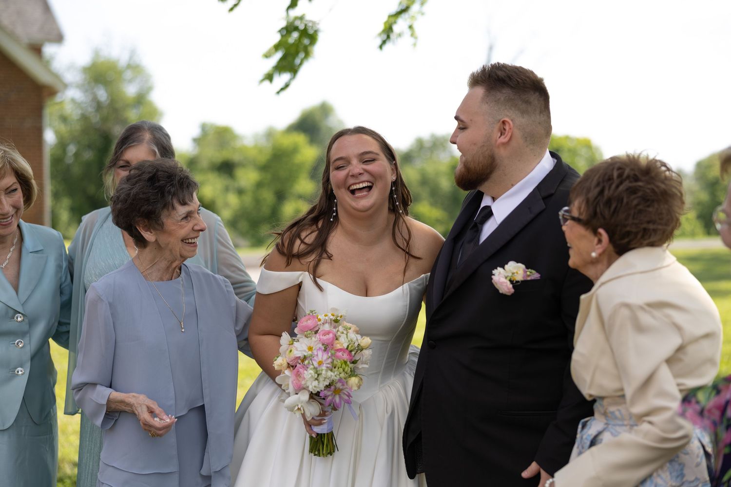 Wedding celebration outdoors with joyful group gathered on sunny summer day.