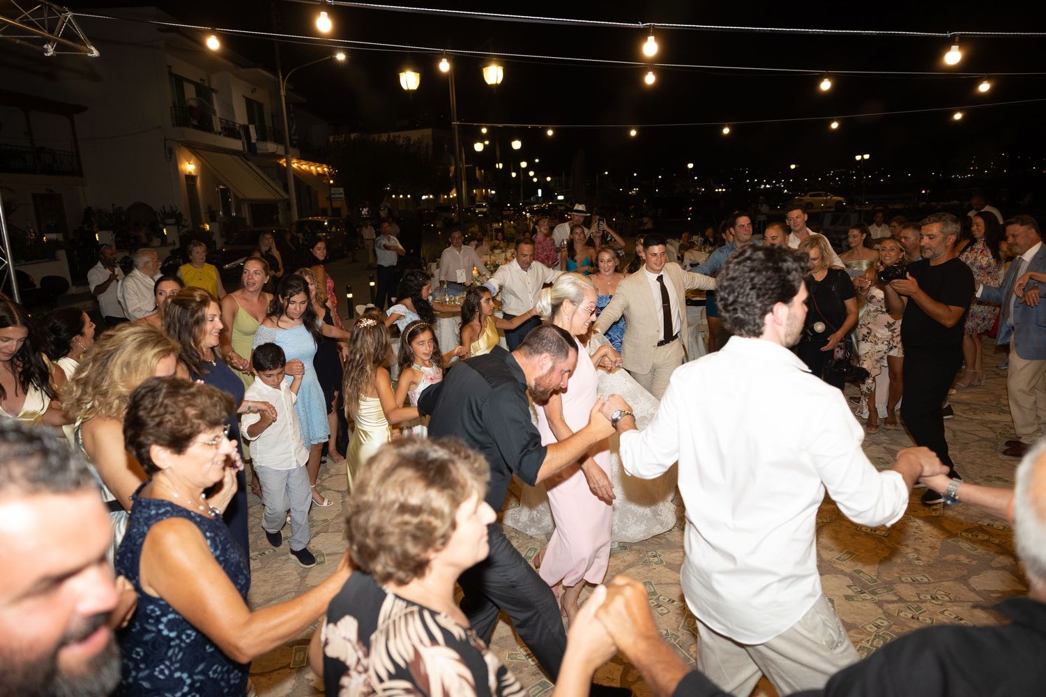 A crowded dance floor with string lights overhead as people celebrate at an evening event.