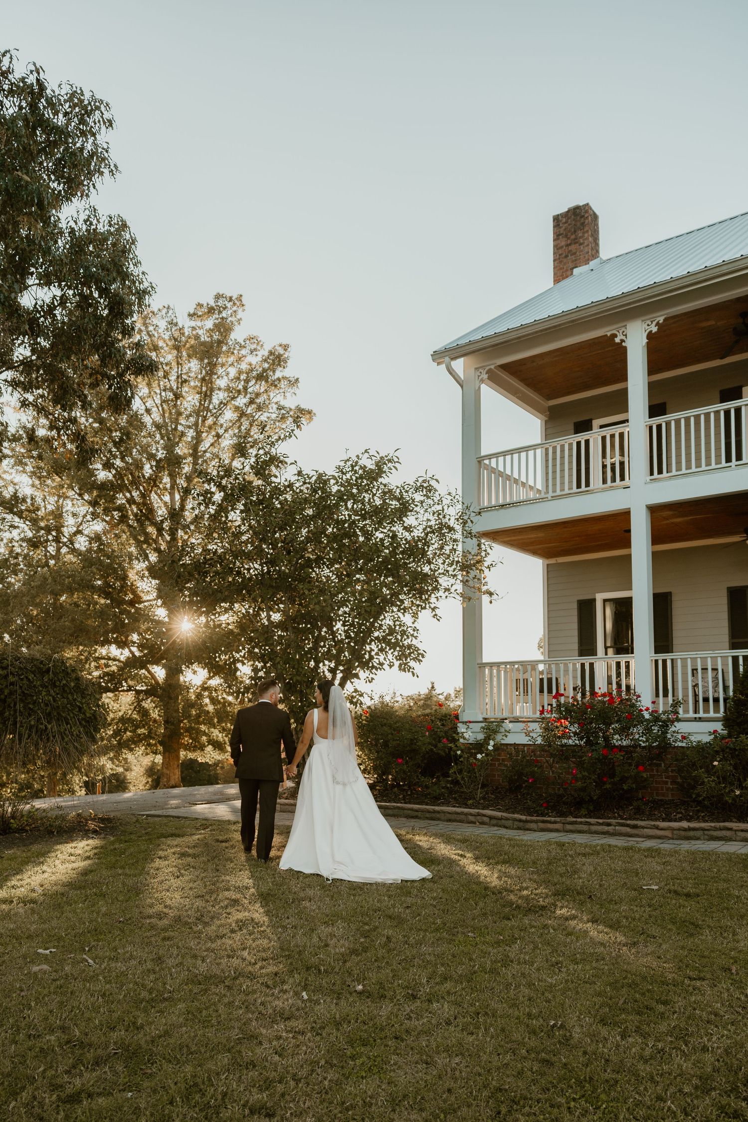 A wedding couple poses at sunset in front of a historic white house with two-story porch.