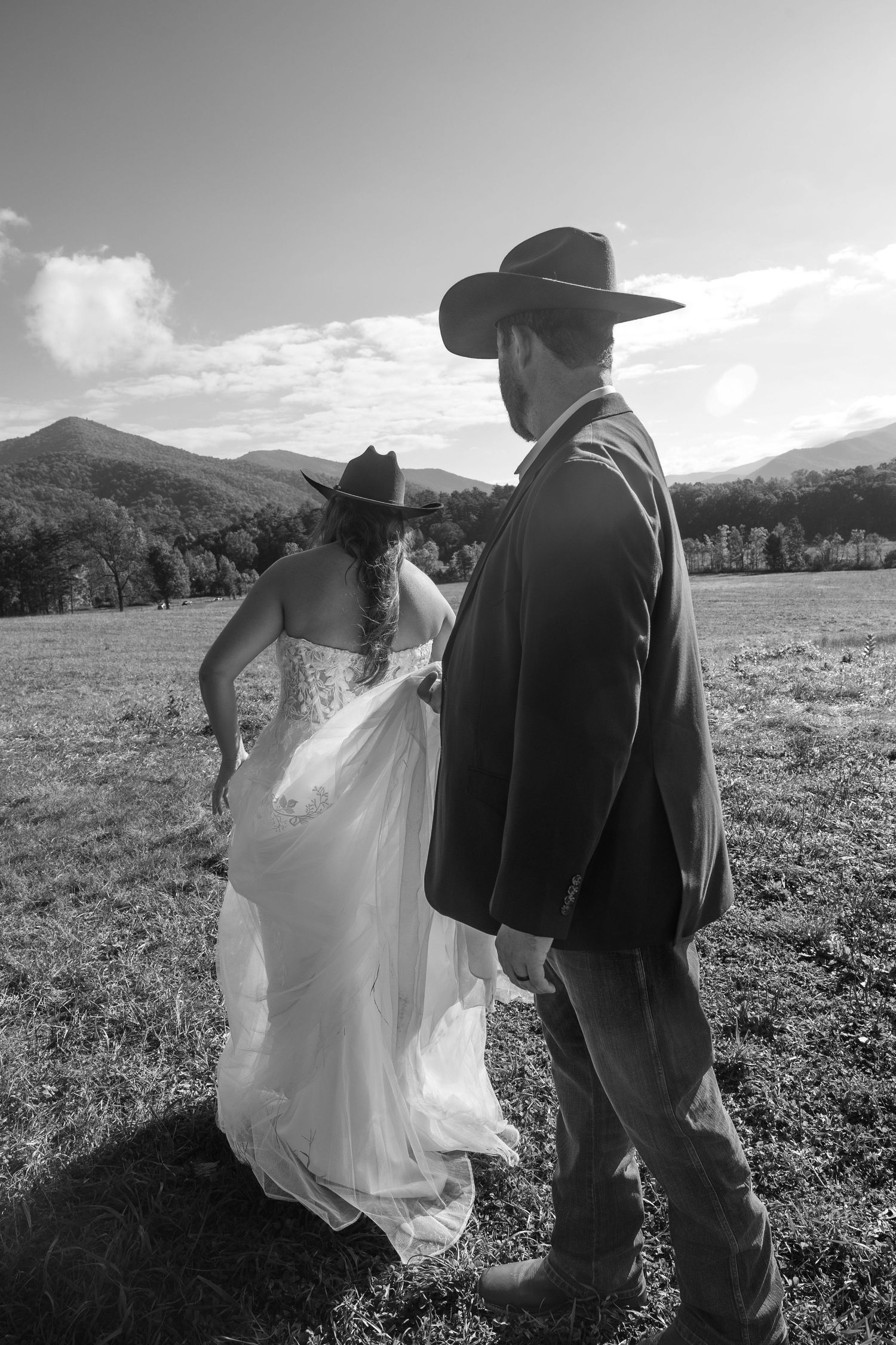 Black and white wedding portrait in a field with mountains and cloudy sky.