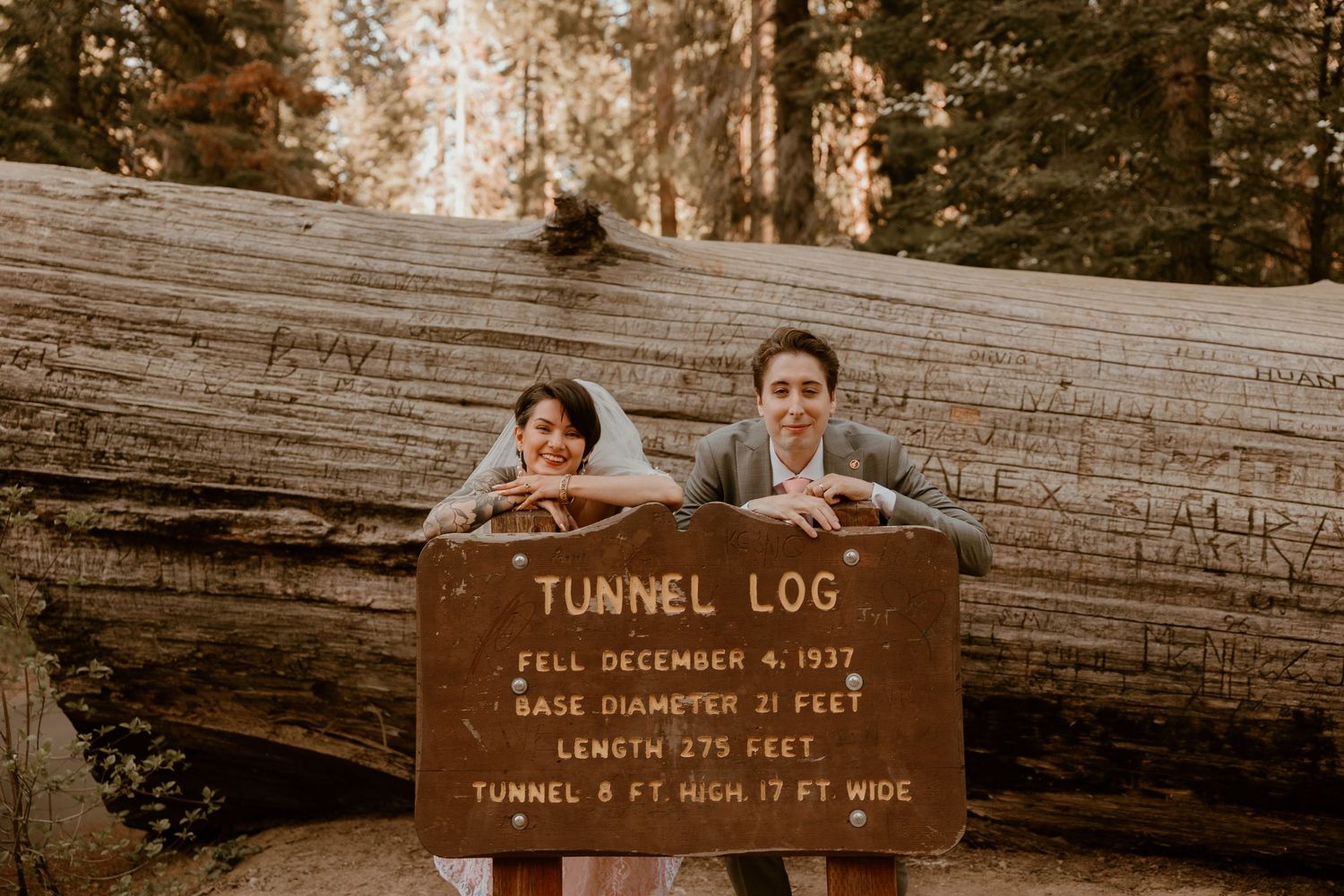 A couple poses behind the Tunnel Log sign in Sequoia National Park.