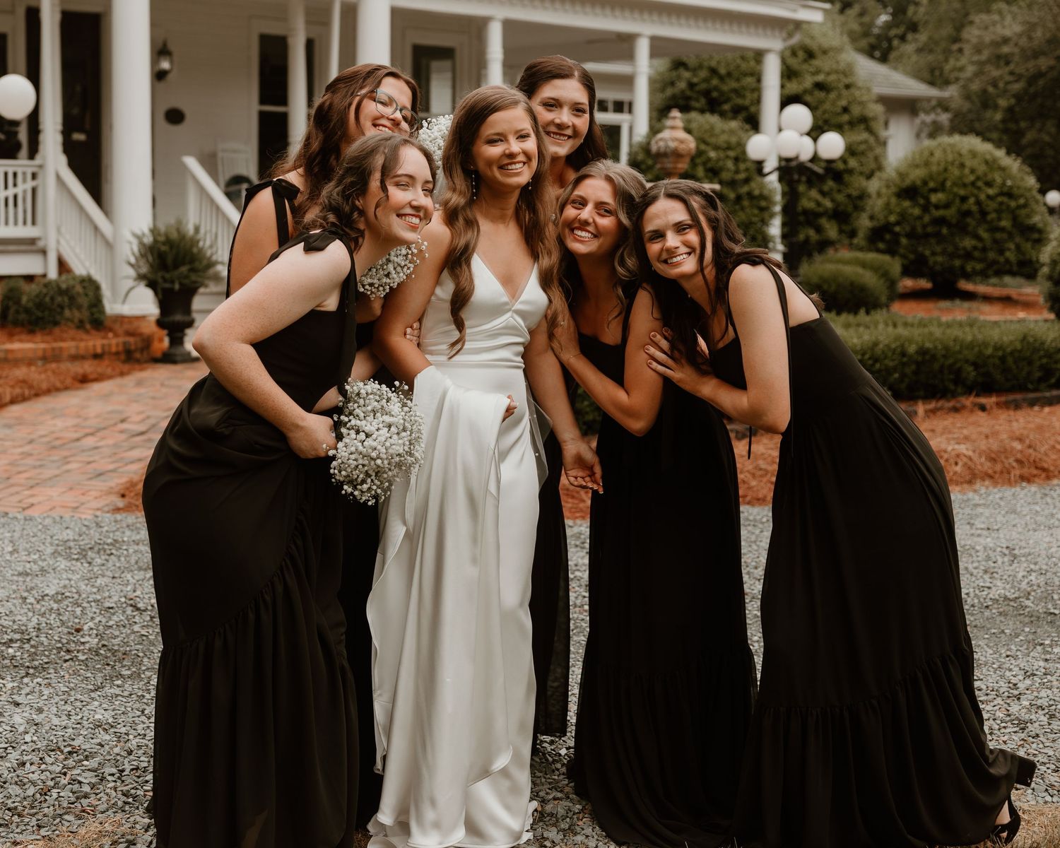 Wedding party poses together with bridesmaids in black dresses and bride in white dress.
