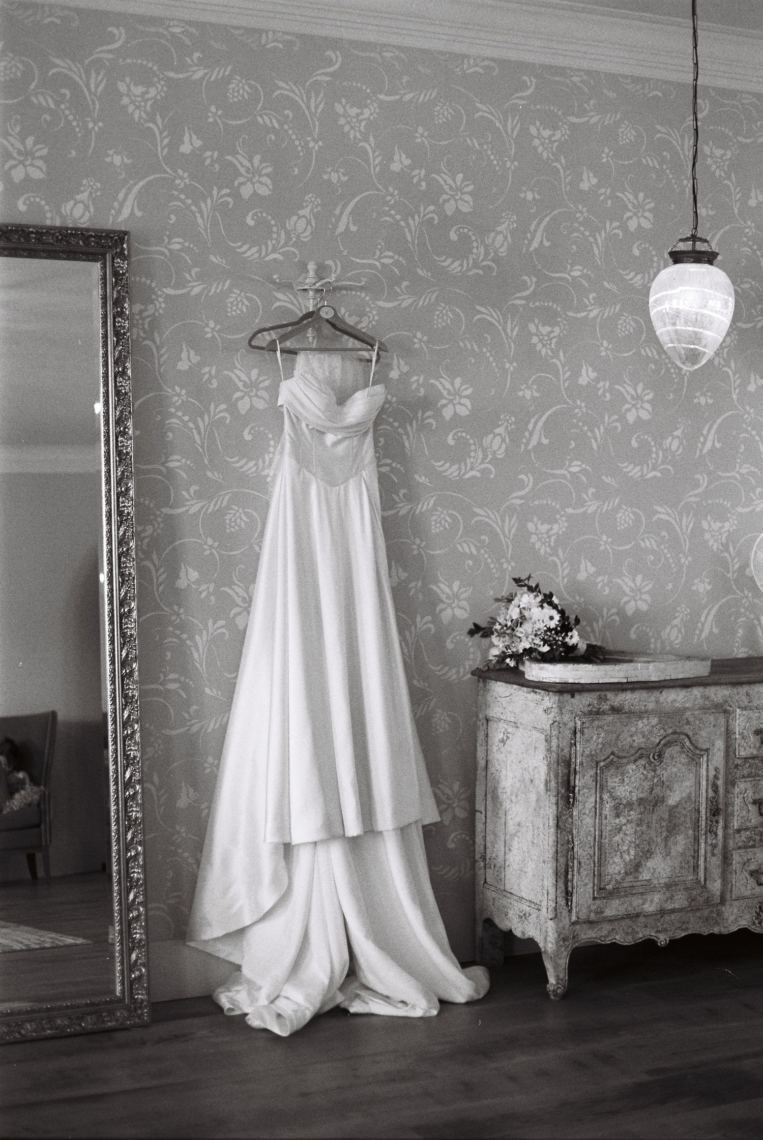 A white wedding dress displayed in different angles against a gray floral wallpapered room with vintage decor.