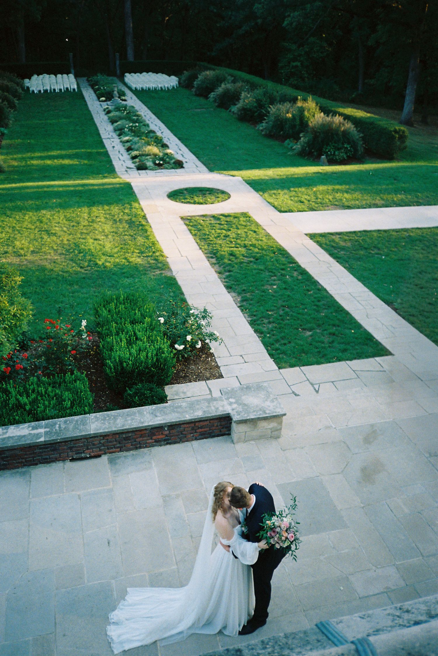 Aerial view of a couple in formal attire walking along geometric garden paths with manicured lawns.