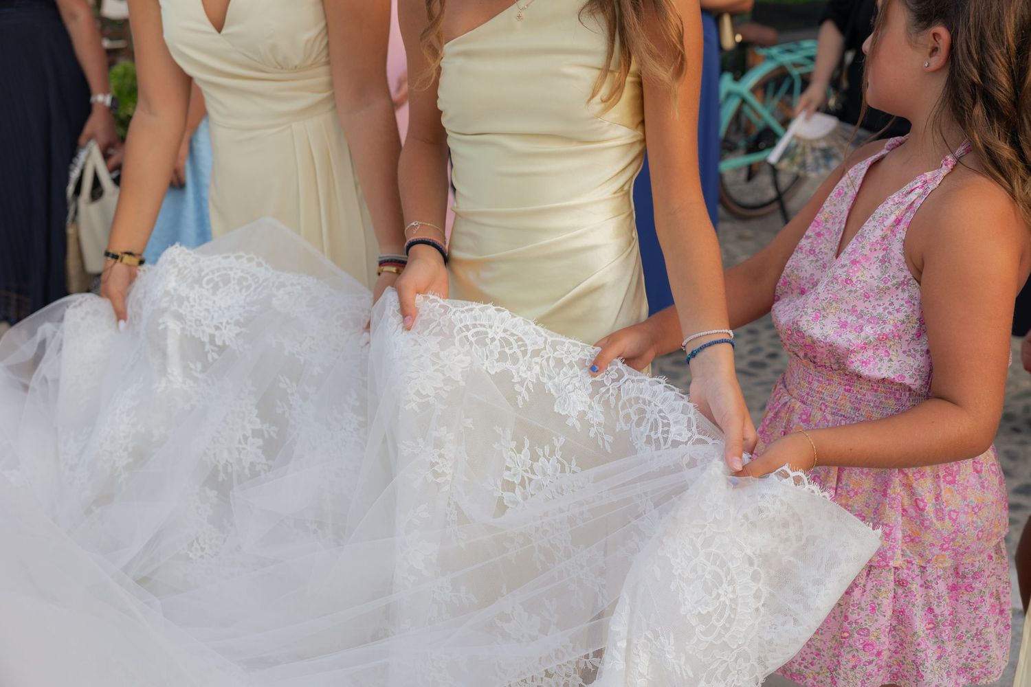 A detailed white wedding dress with lace and tulle being held alongside yellow bridesmaid dresses at a wedding.