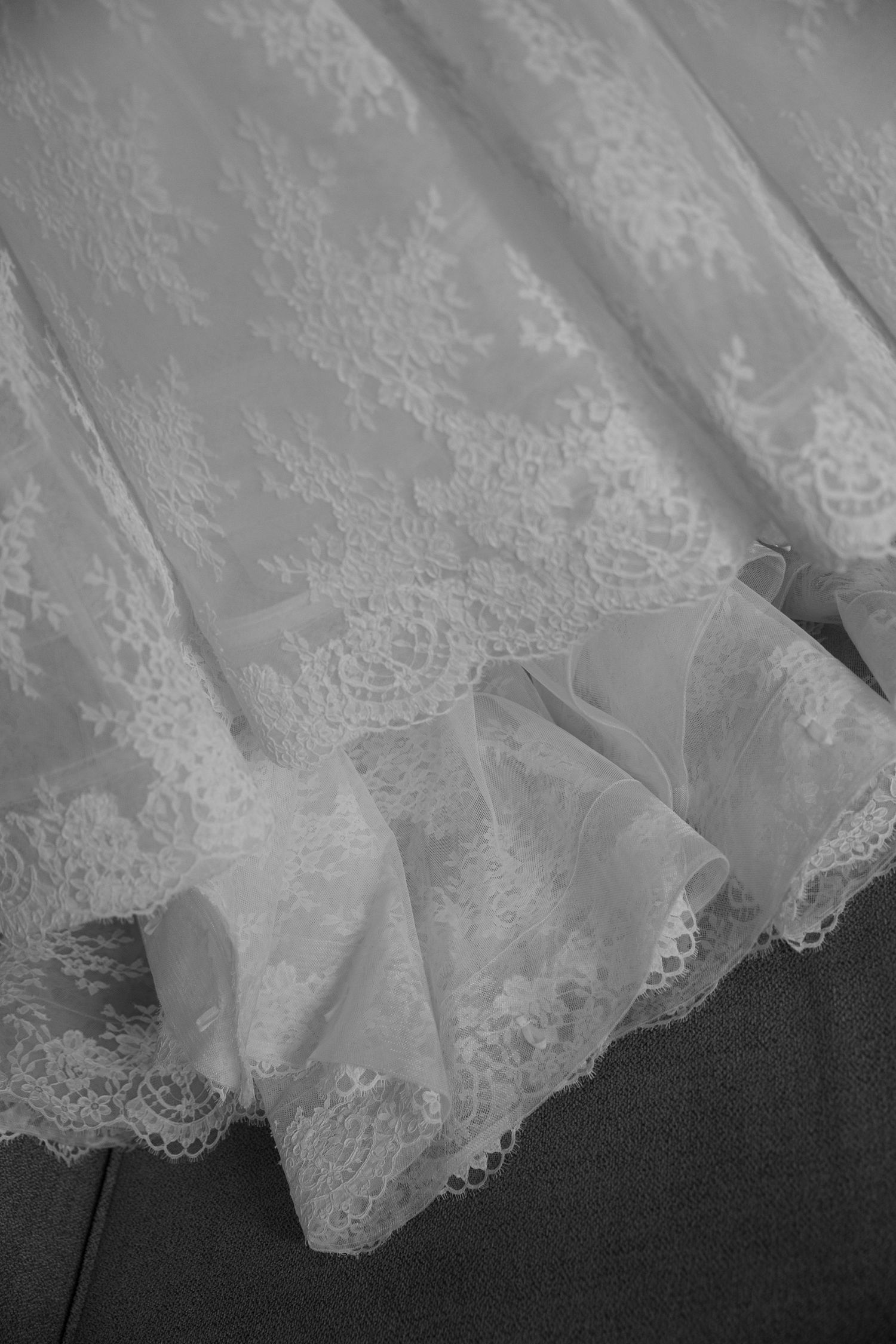 Close-up detail of delicate white lace trim and tulle fabric from a wedding dress laying on dark floor.