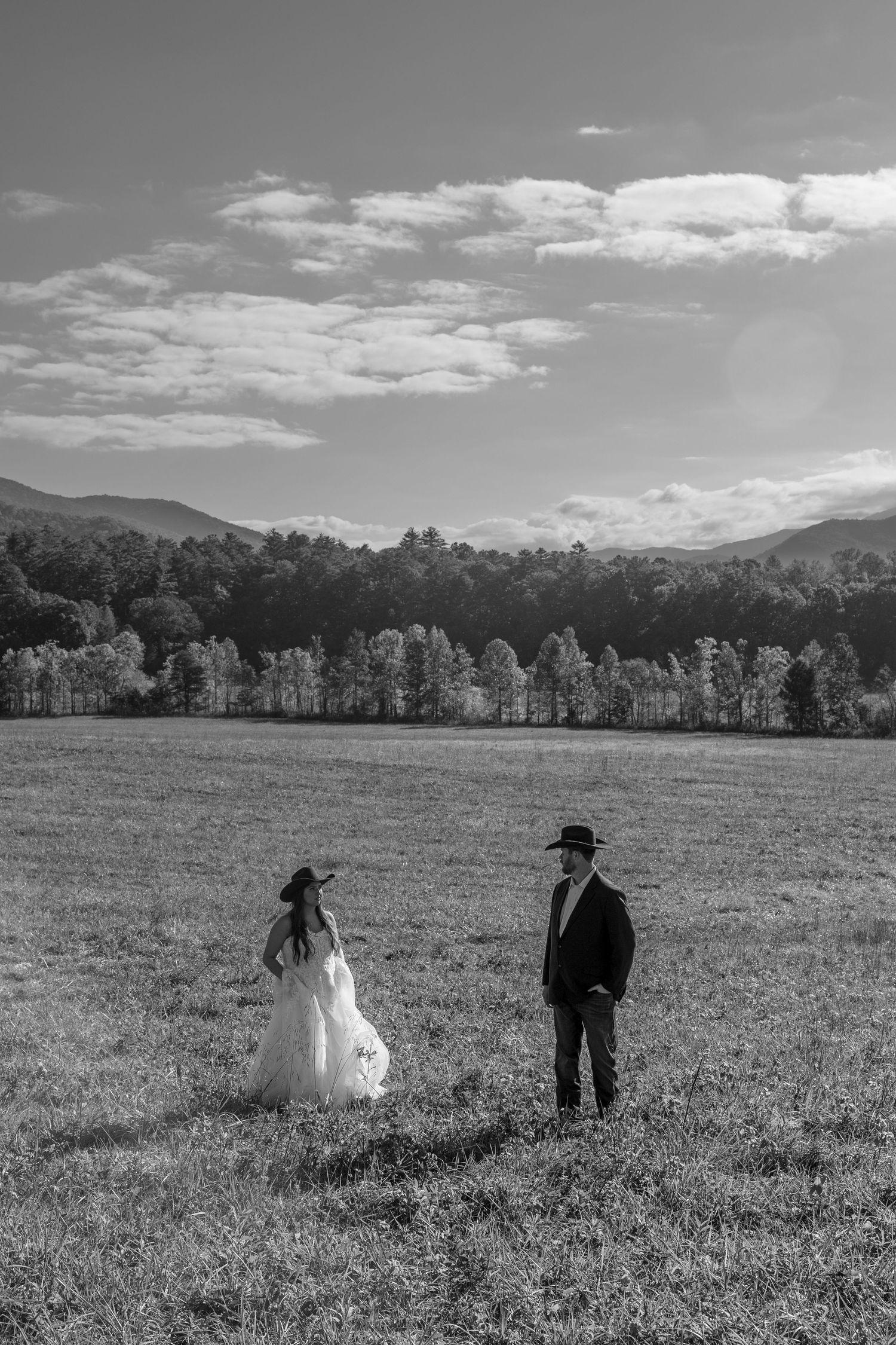 Black and white landscape of couple in wedding attire standing in vast mountain field.