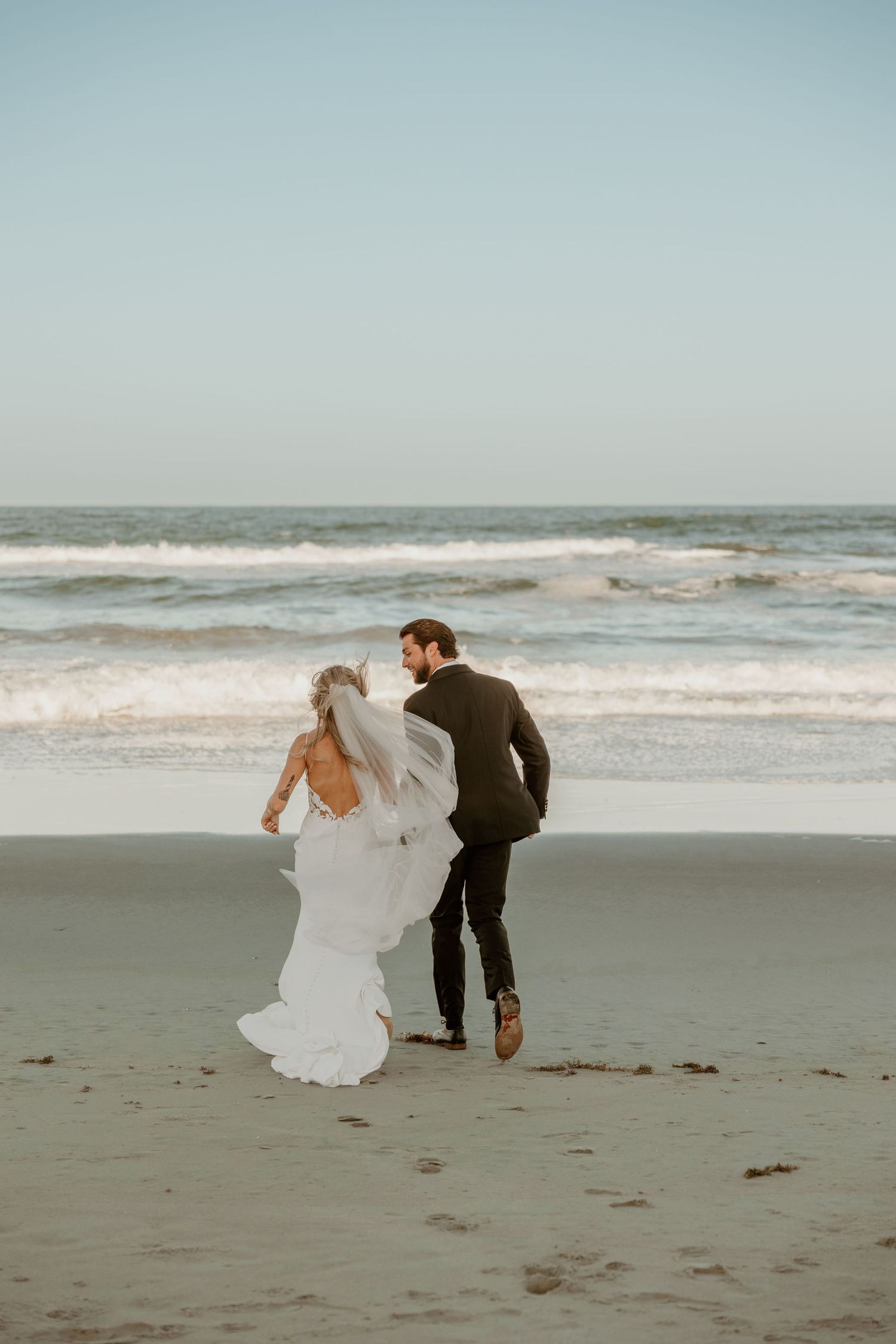 A couple walks along the shoreline with ocean waves and mist creating a dreamy backdrop.