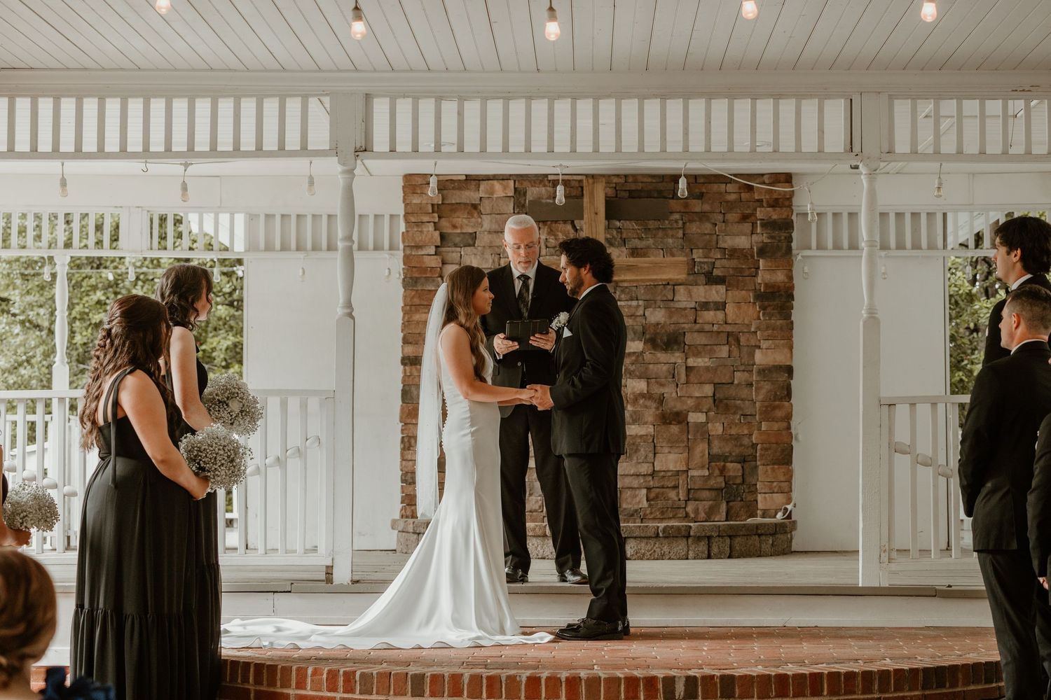 Wedding ceremony taking place in a white pavilion with stone fireplace backdrop.