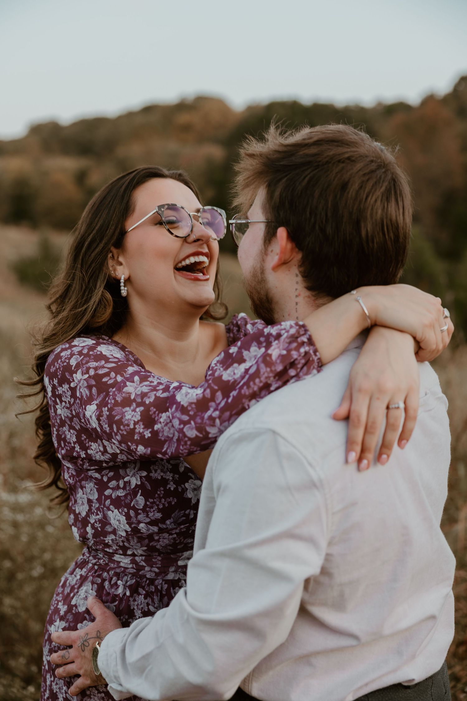 Joyful couple laughing together during outdoor engagement photo session in autumn field.