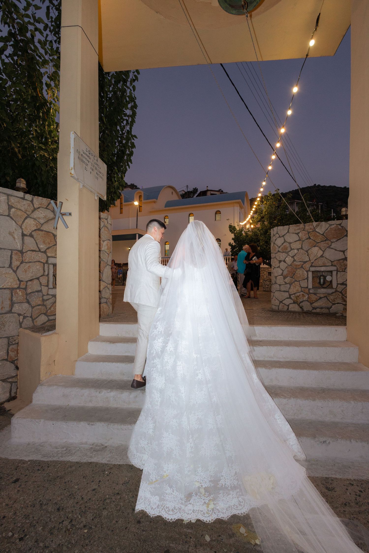 Two white wedding dresses displayed on dress forms under outdoor patio lighting at dusk.