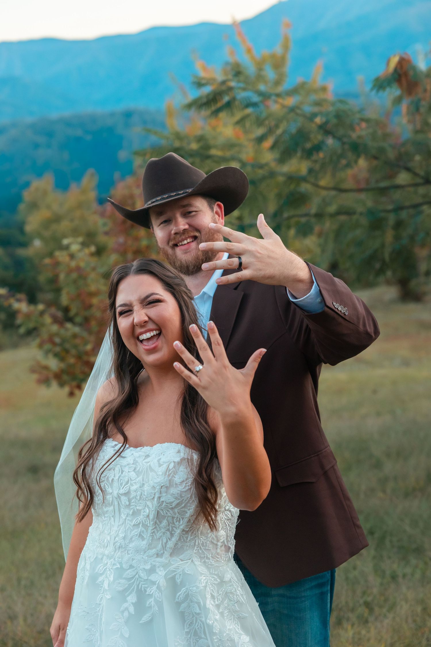A joyful wedding couple poses together in front of mountain scenery.