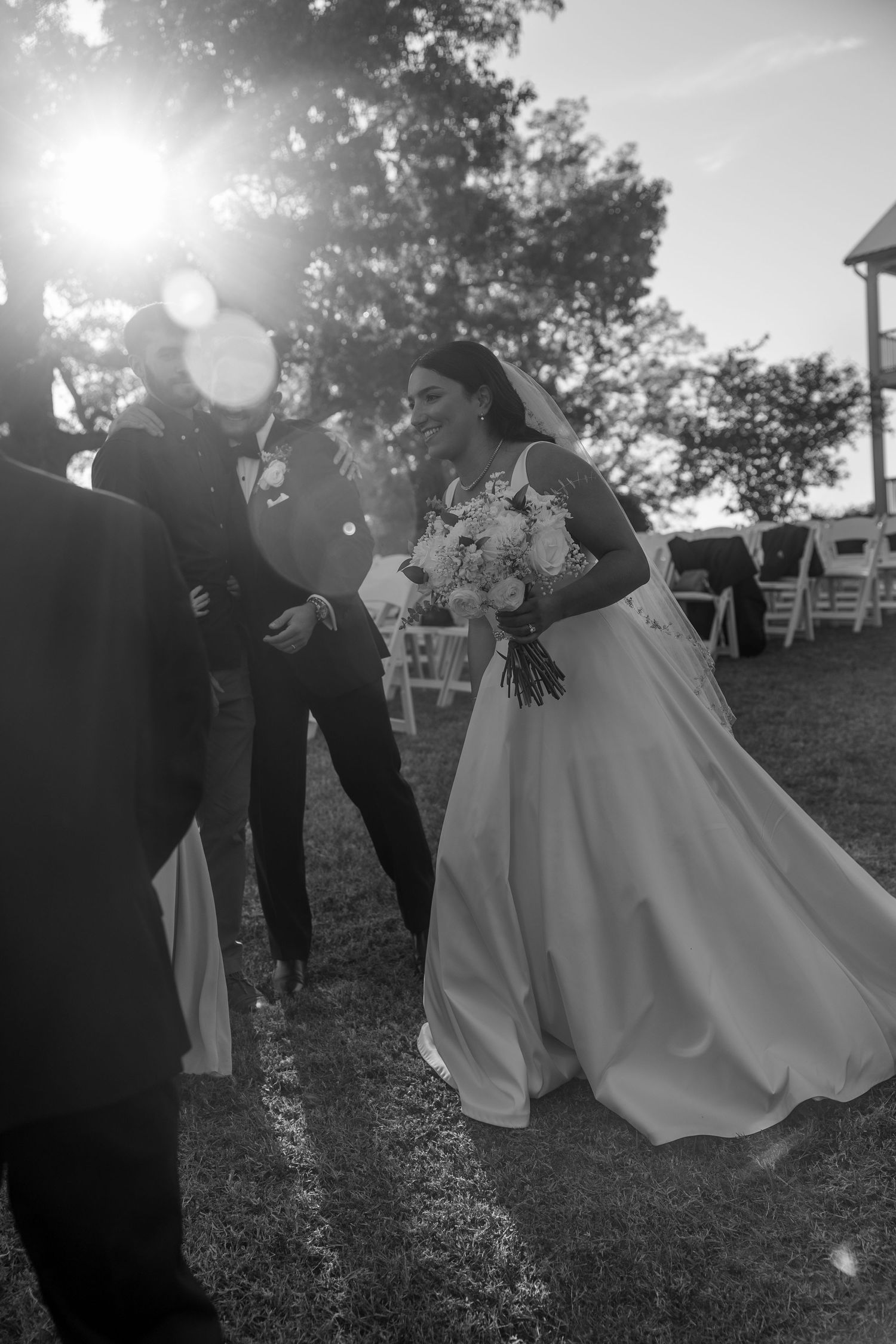 Black and white photo of a wedding ceremony with sunlight flares and bride holding a bouquet.
