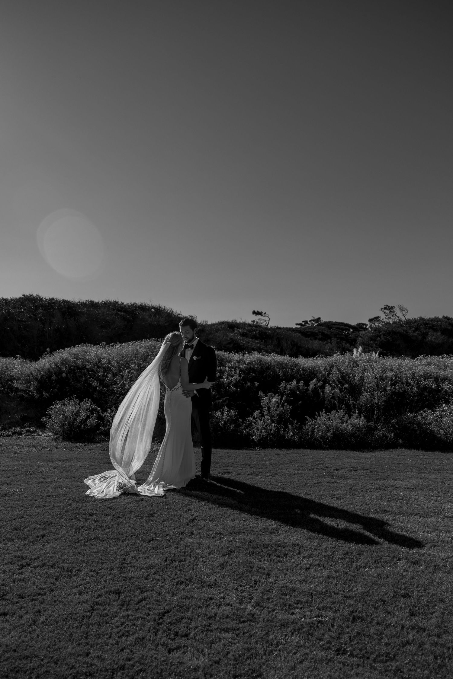 Black and white landscape shot of a wedding couple creating long shadows on grassy terrain.