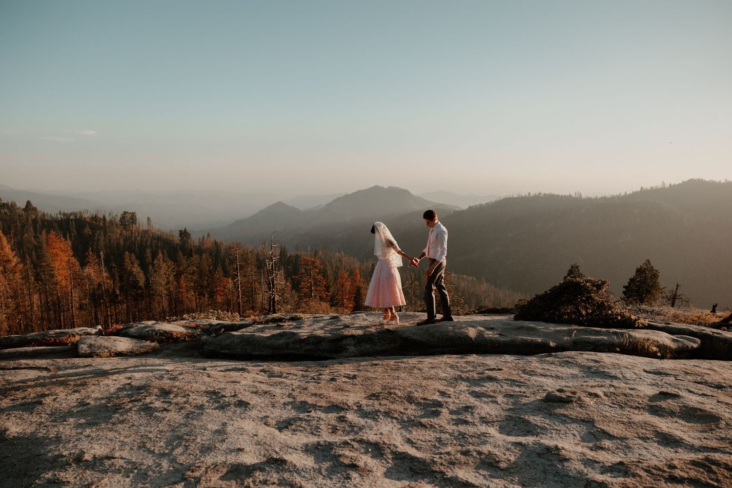 Couple shares tender moment on rocky mountain peak during golden hour.