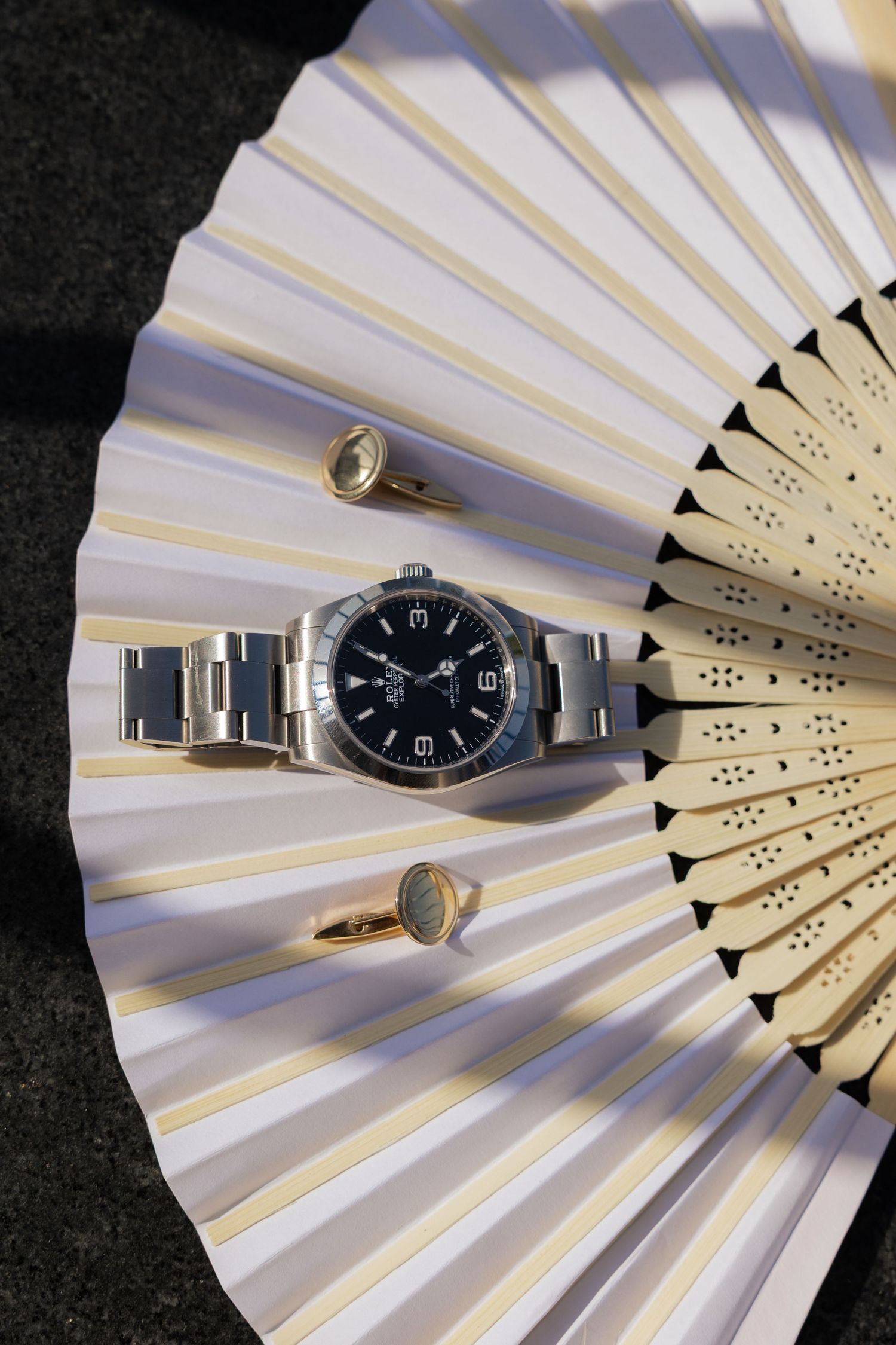 Silver wristwatch displayed artistically on a white folding fan against black background.