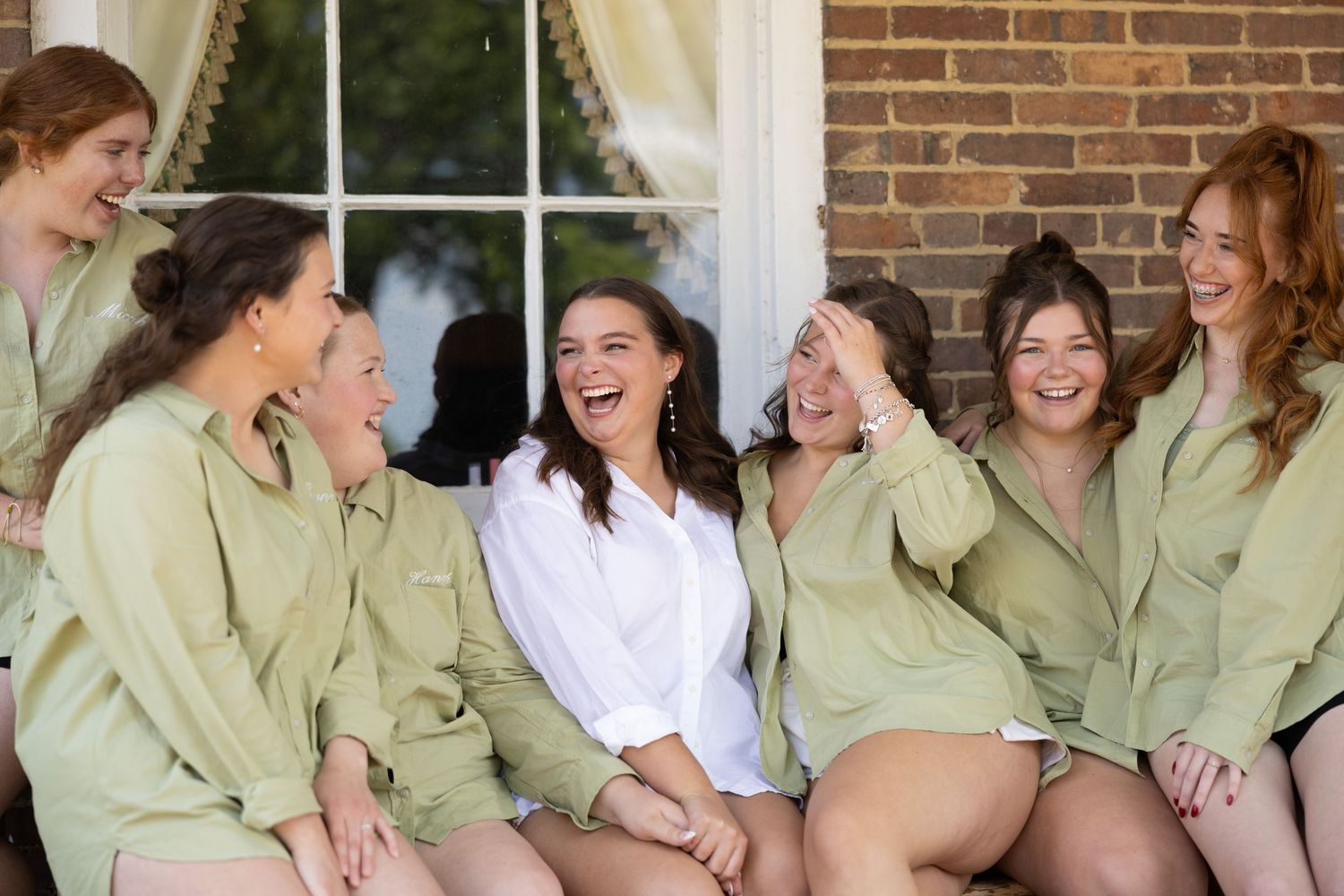 A group wearing sage green robes sitting together on a porch, sharing laughter and smiles.