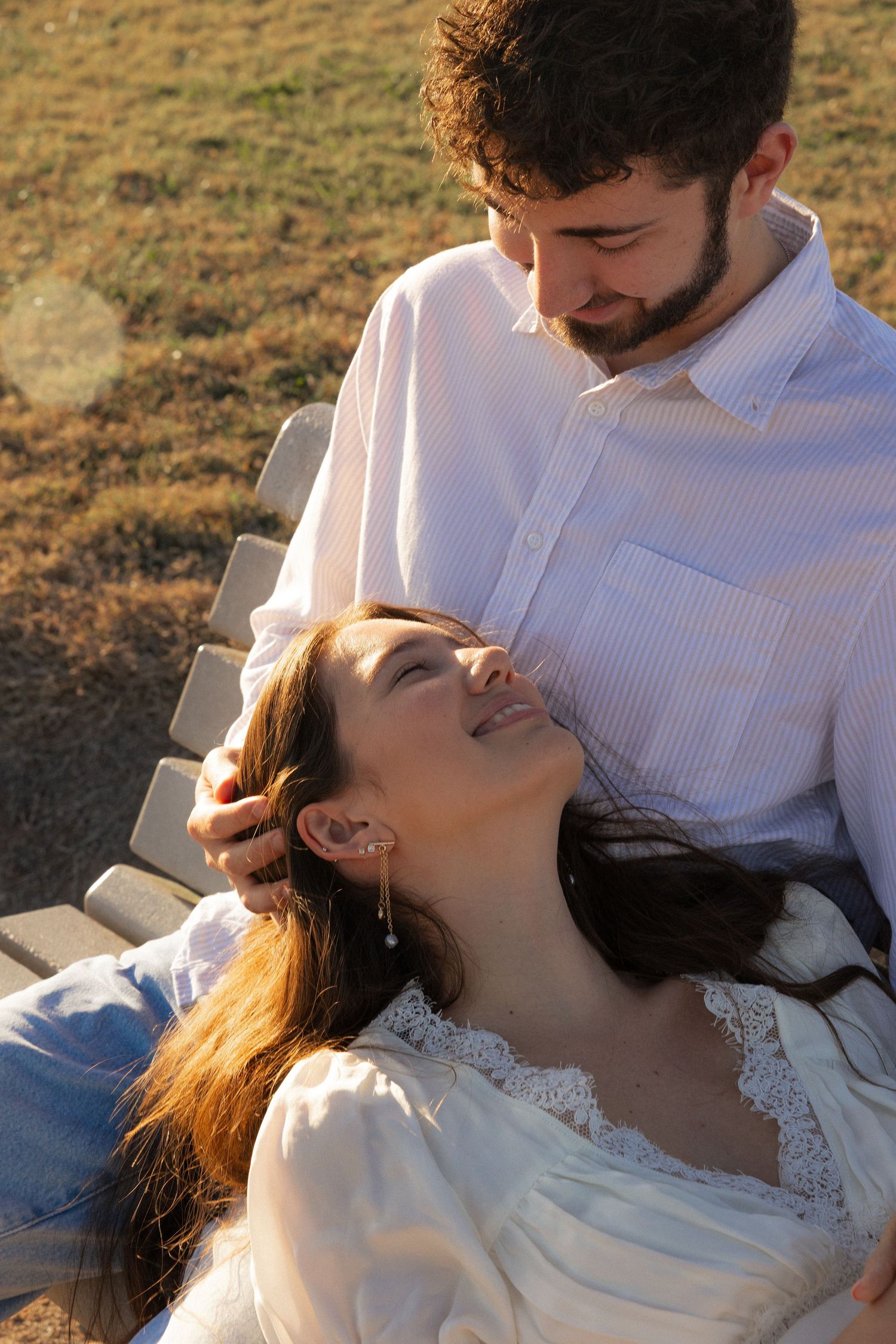 A romantic couple embraces during a sunset photoshoot in a field wearing white and beige clothing.