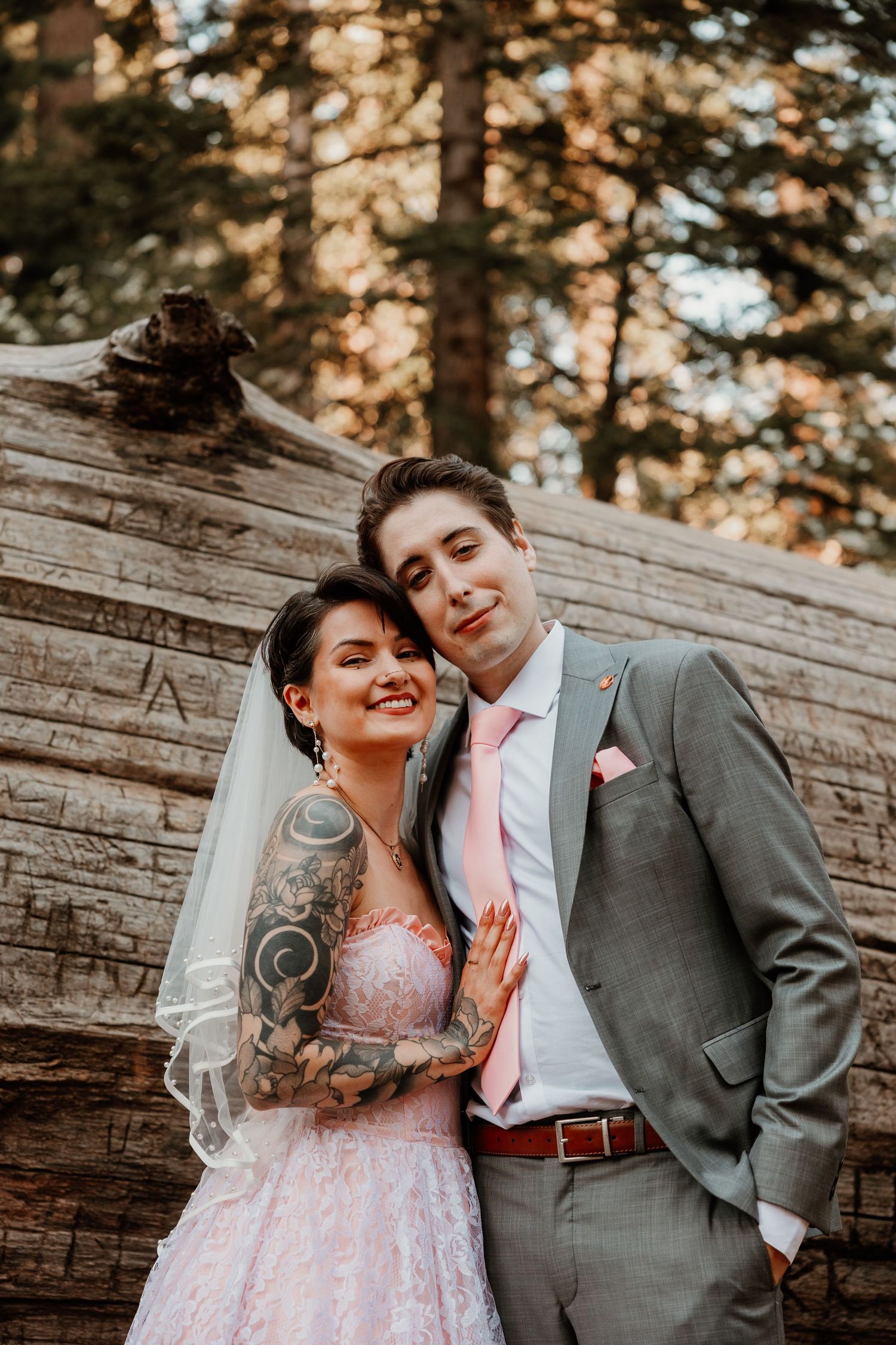 A wedding couple posing against a fallen log in a redwood forest.