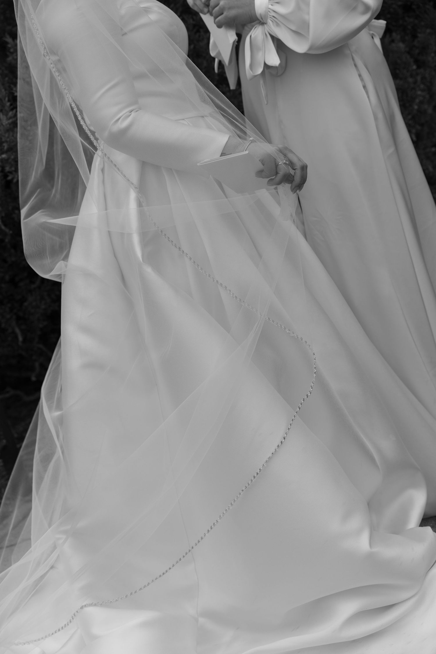 Close-up details of a flowing white wedding dress with delicate beading and fabric textures against a dark background.
