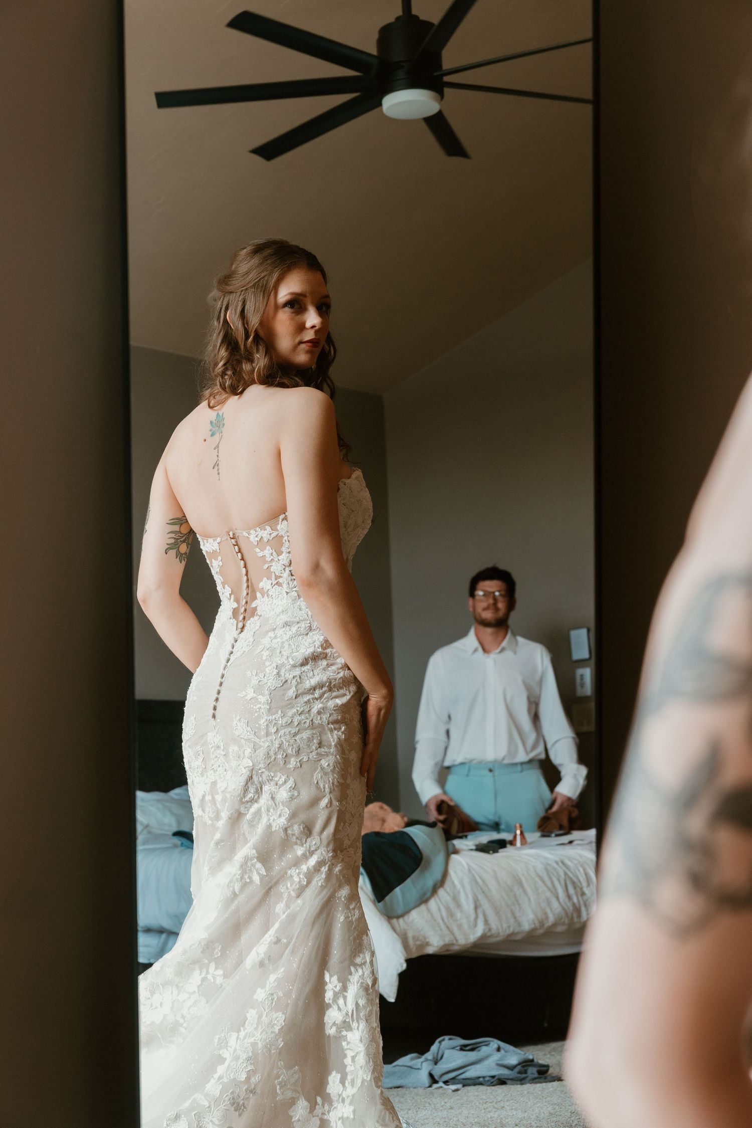 A wedding dress fitting scene showing the detailed back of a lace gown.