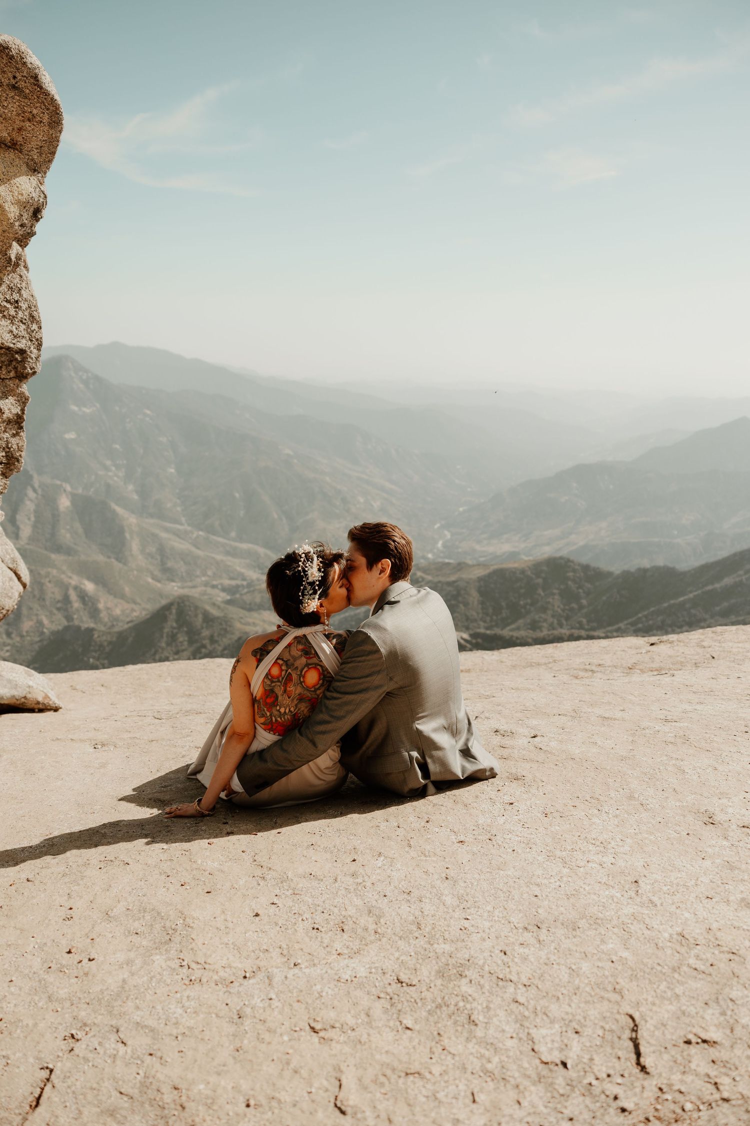 A romantic couple lying on a mountain summit with sweeping valley views in the background.