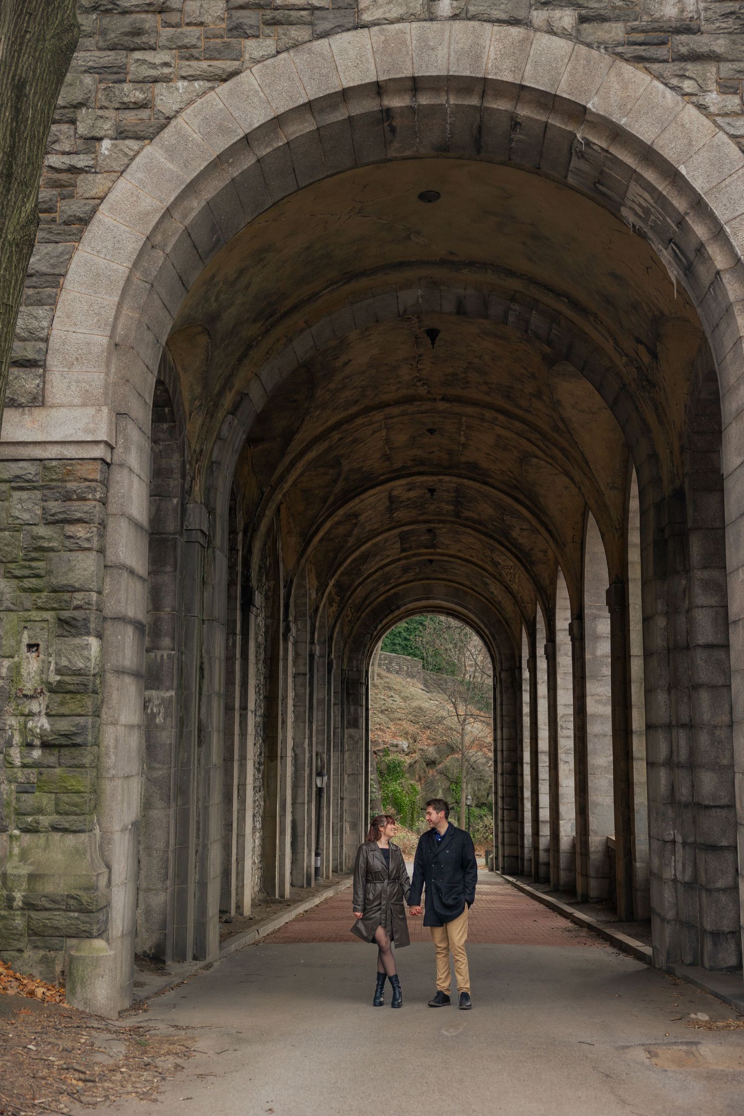 A couple walks through a grand stone archway tunnel with beautiful architectural details.