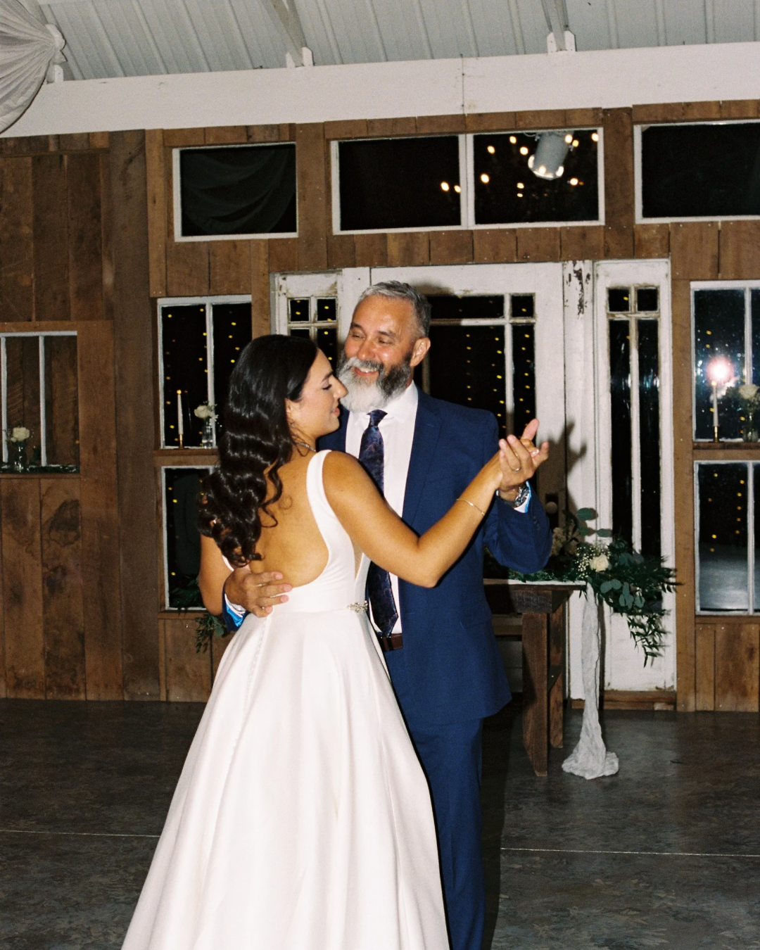 Newlyweds share their first dance in an elegant wooden barn venue with romantic lighting.
