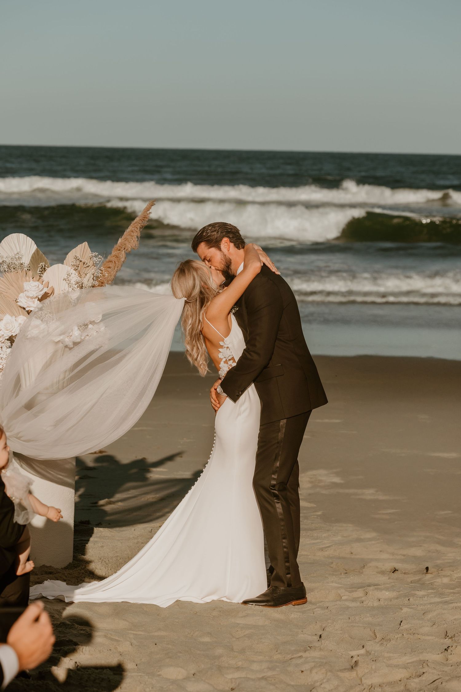 A romantic beach wedding ceremony with flowing veil and crashing waves in the background.