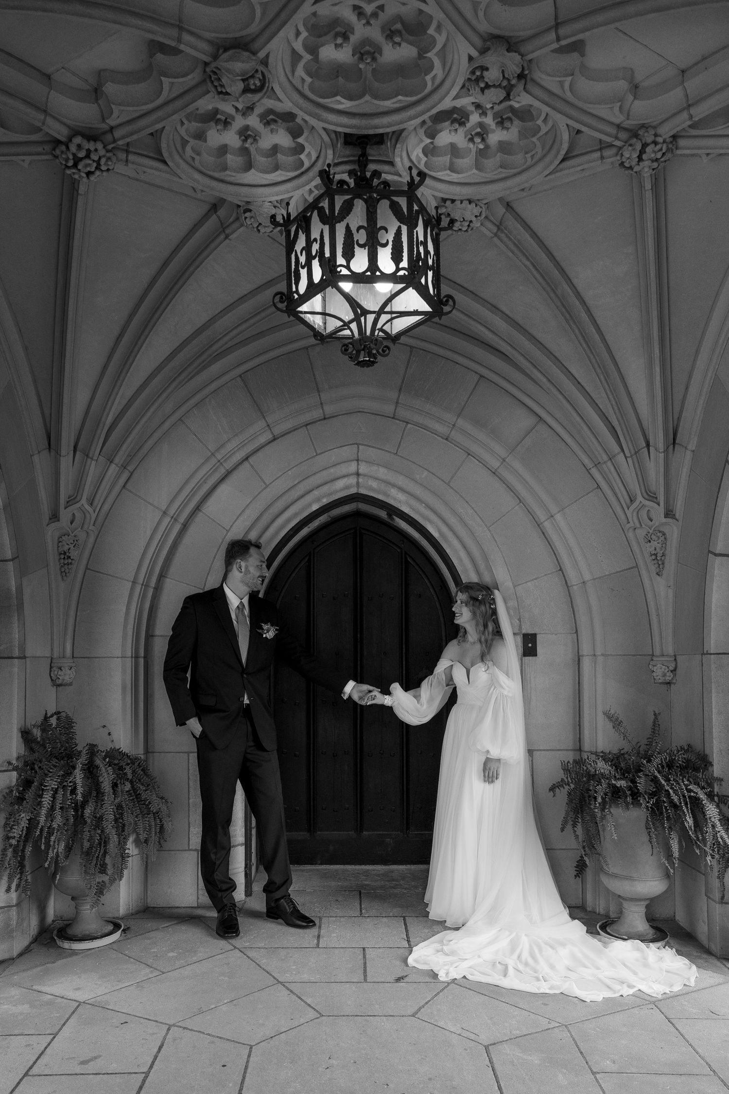 Black and white wedding photos captured in ornate gothic archway with hanging chandelier.